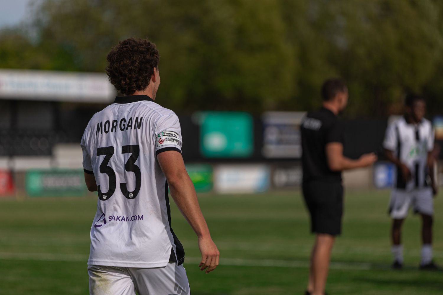 Soccer player wearing Morgan number 33 jersey stands on green pitch during a sunny outdoor football match.
