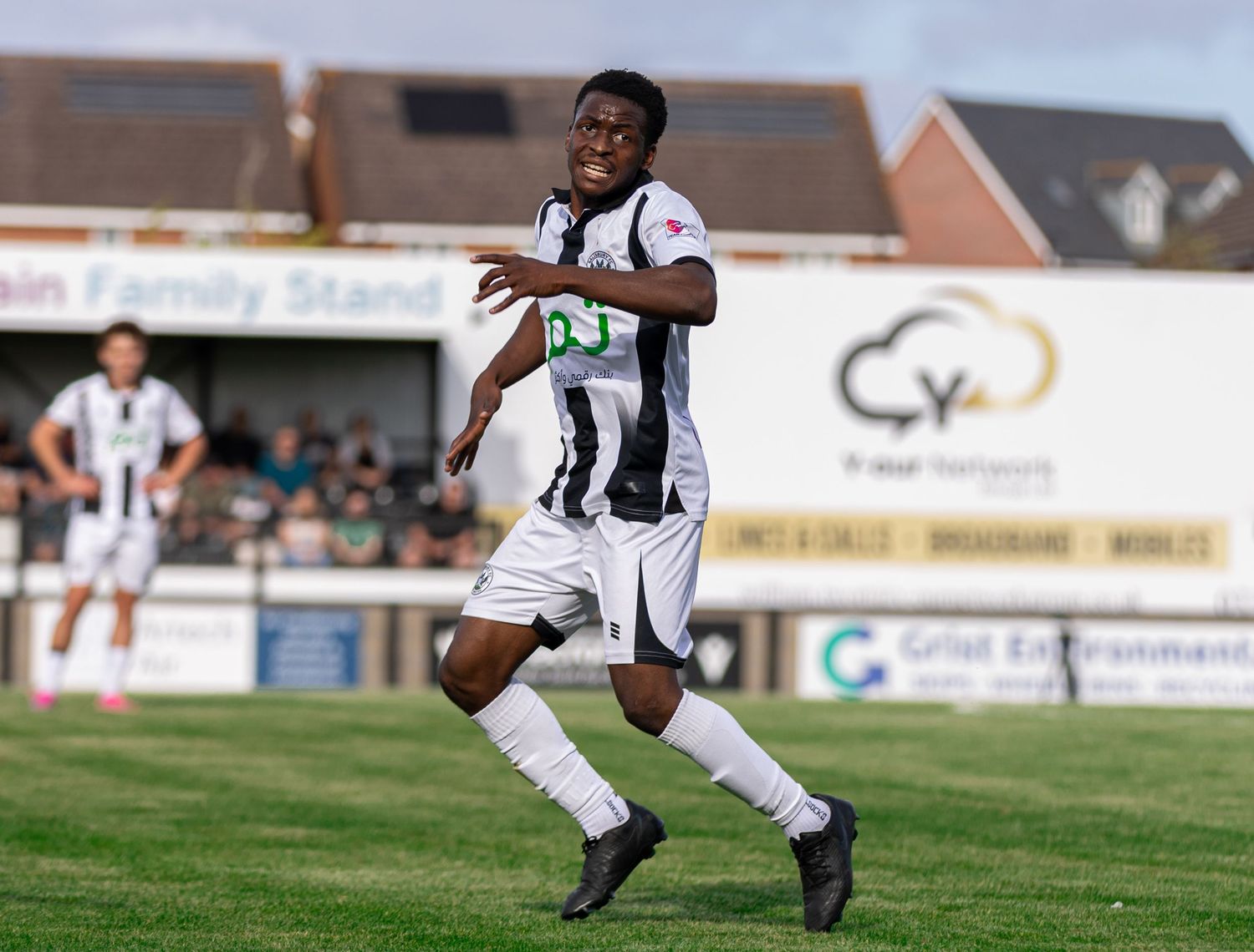 Soccer player in black and white kit sprinting on a green pitch during a sunny match day.