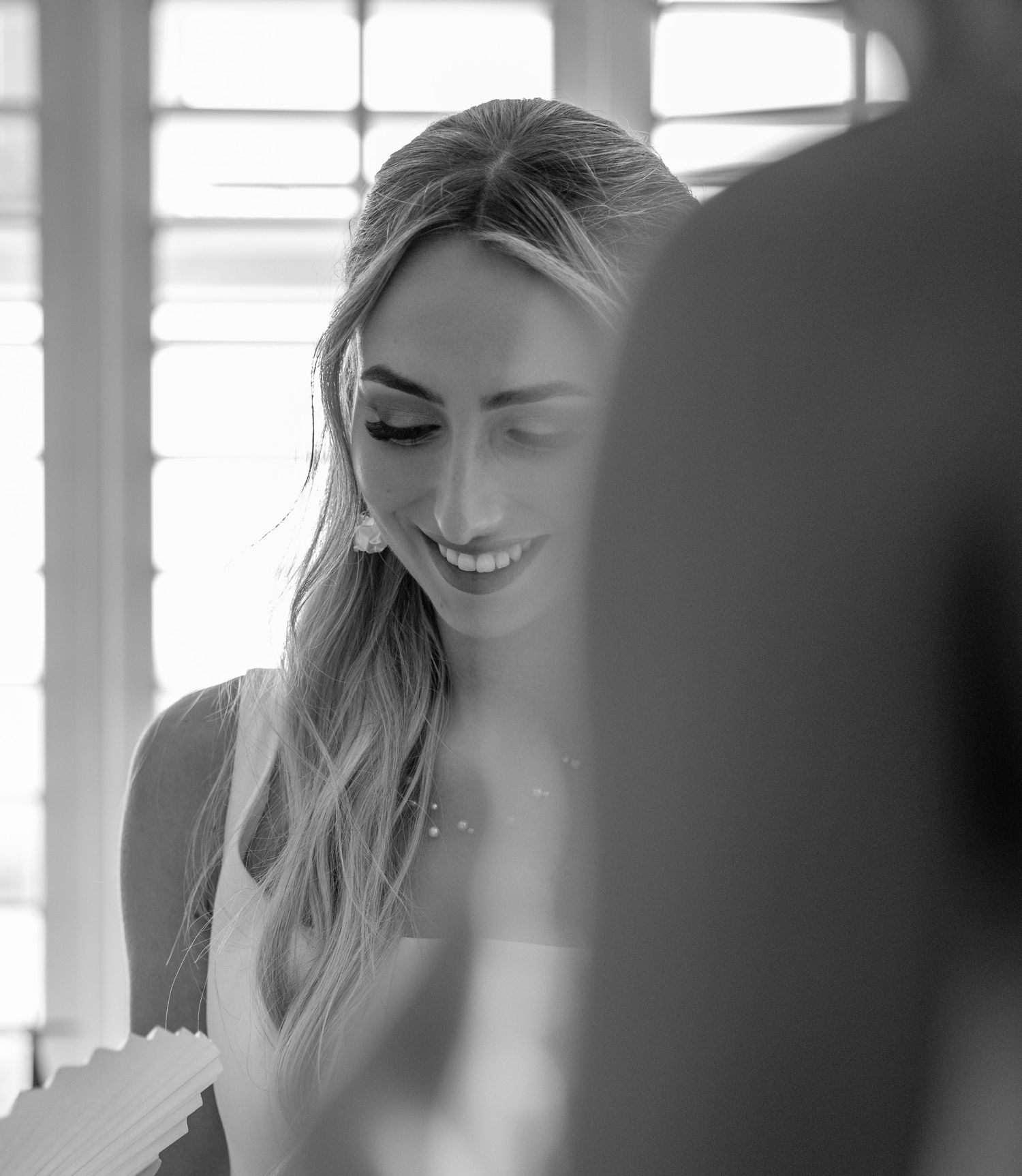 Black and white photo of smiling bride with long wavy hair looking down at wedding papers.