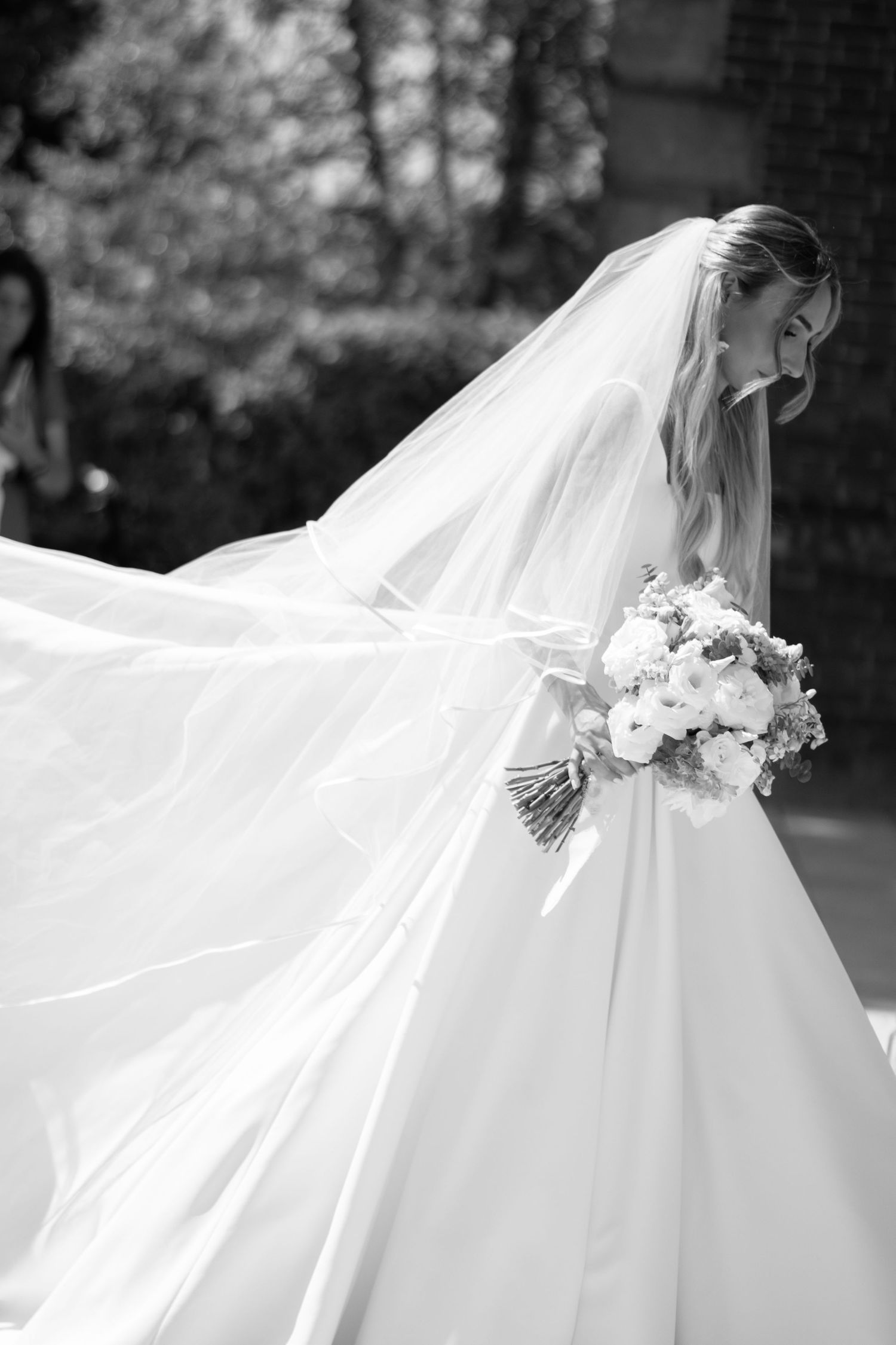 Black and white photo of bride in ball gown with flowing veil and white bouquet.