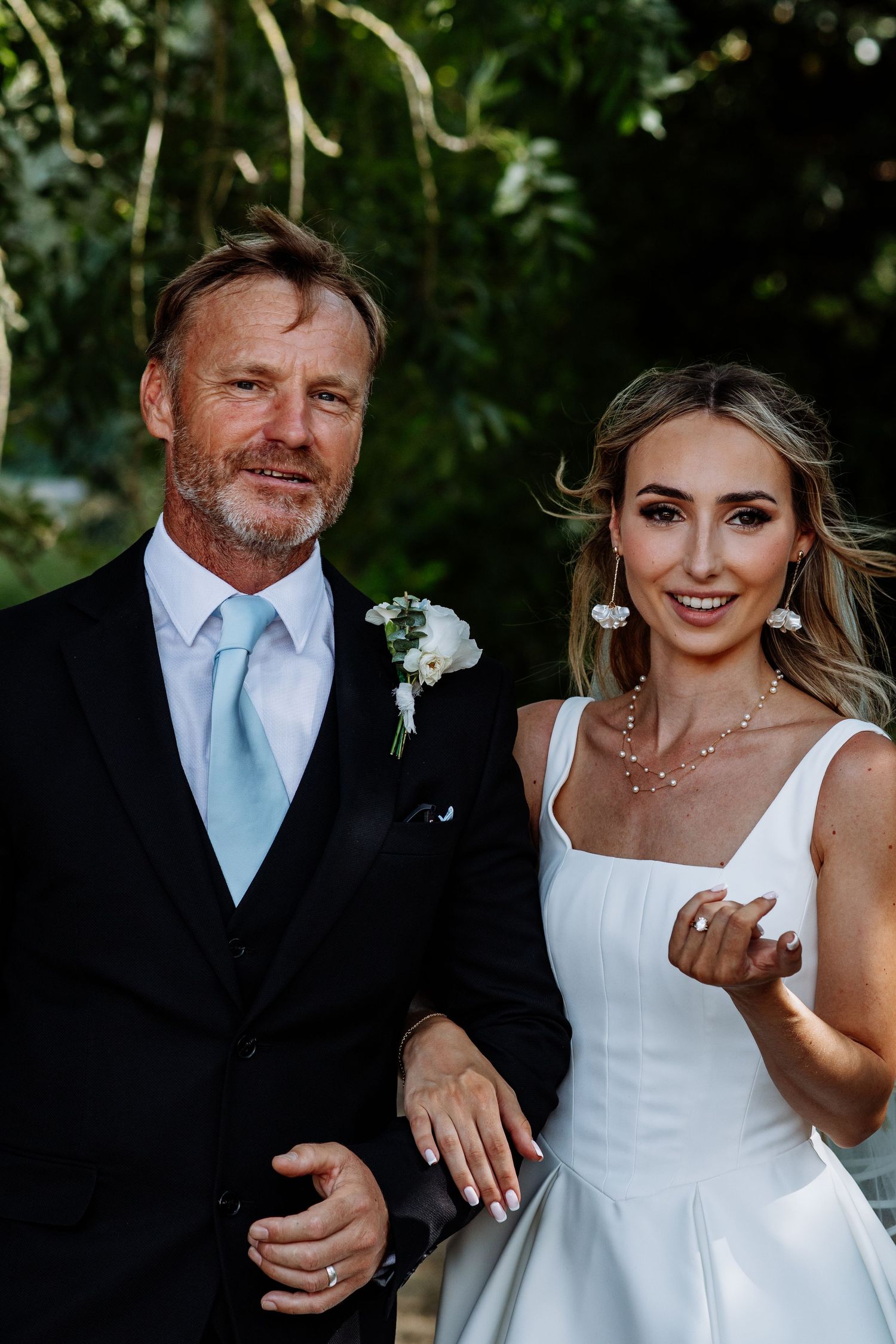 Blonde bride in white wedding dress posing with older gentleman in black suit and light blue tie.