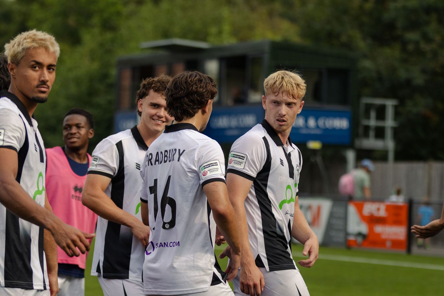 A group of footballers in black and white striped kits celebrate together during a match.