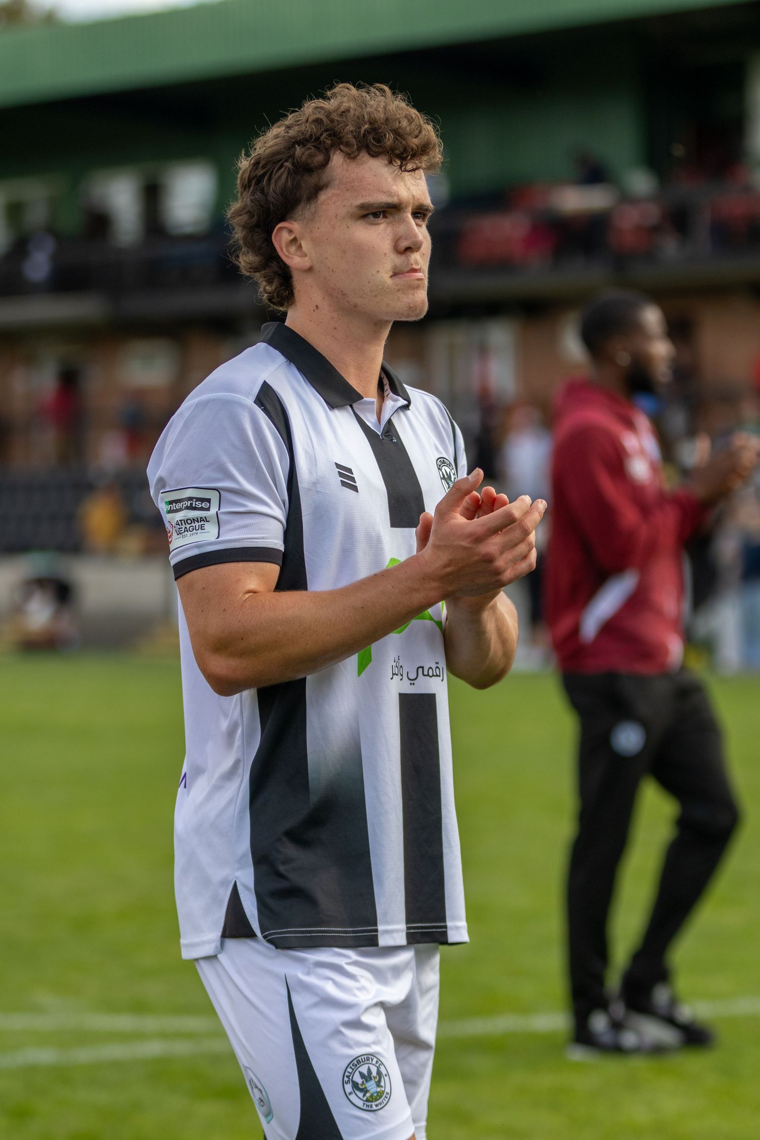 football player in black and white striped jersey applauding fans on the field after a match.