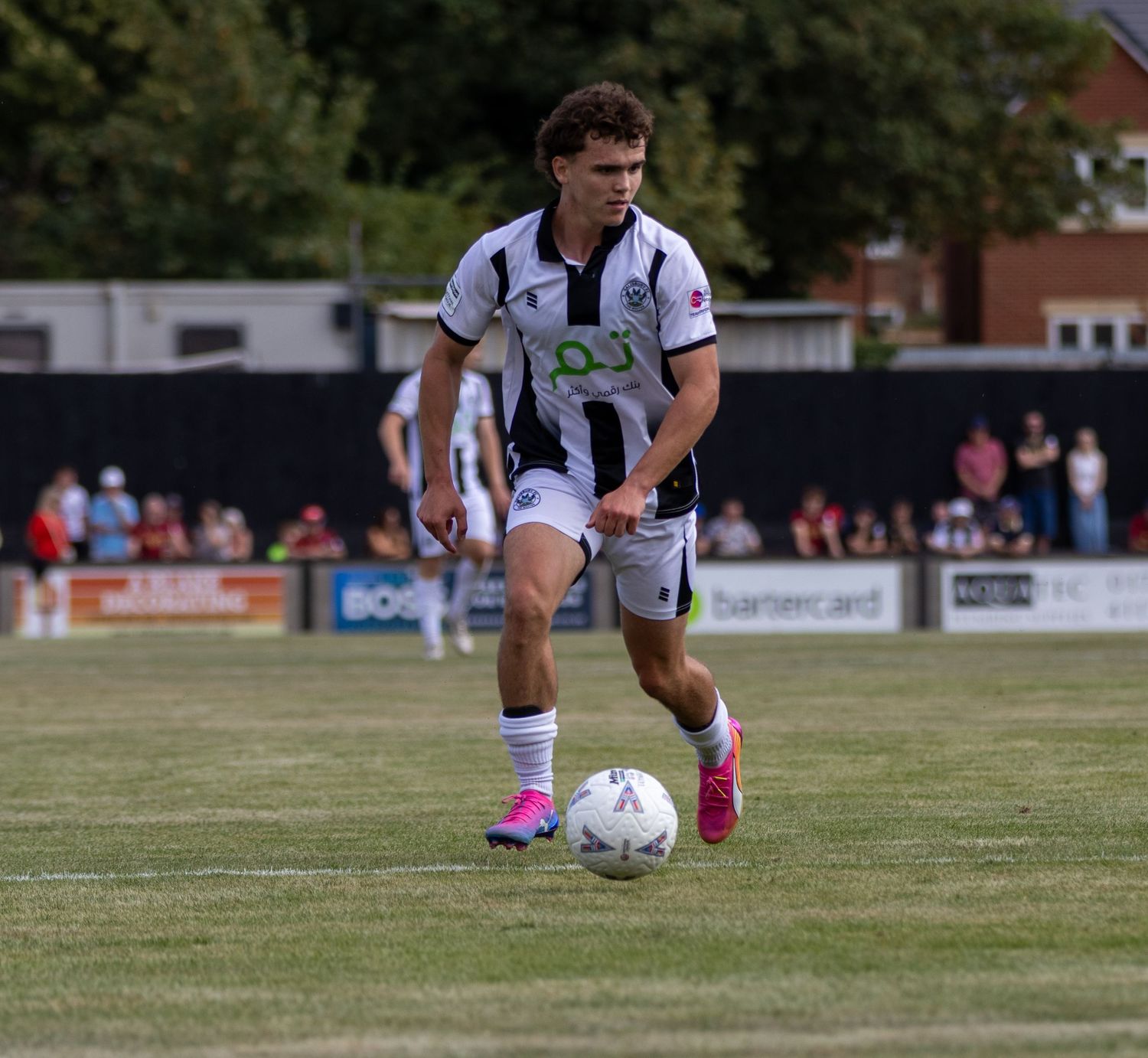 Young footballer in black and white kit dribbles a ball on a grass pitch during a competitive match.