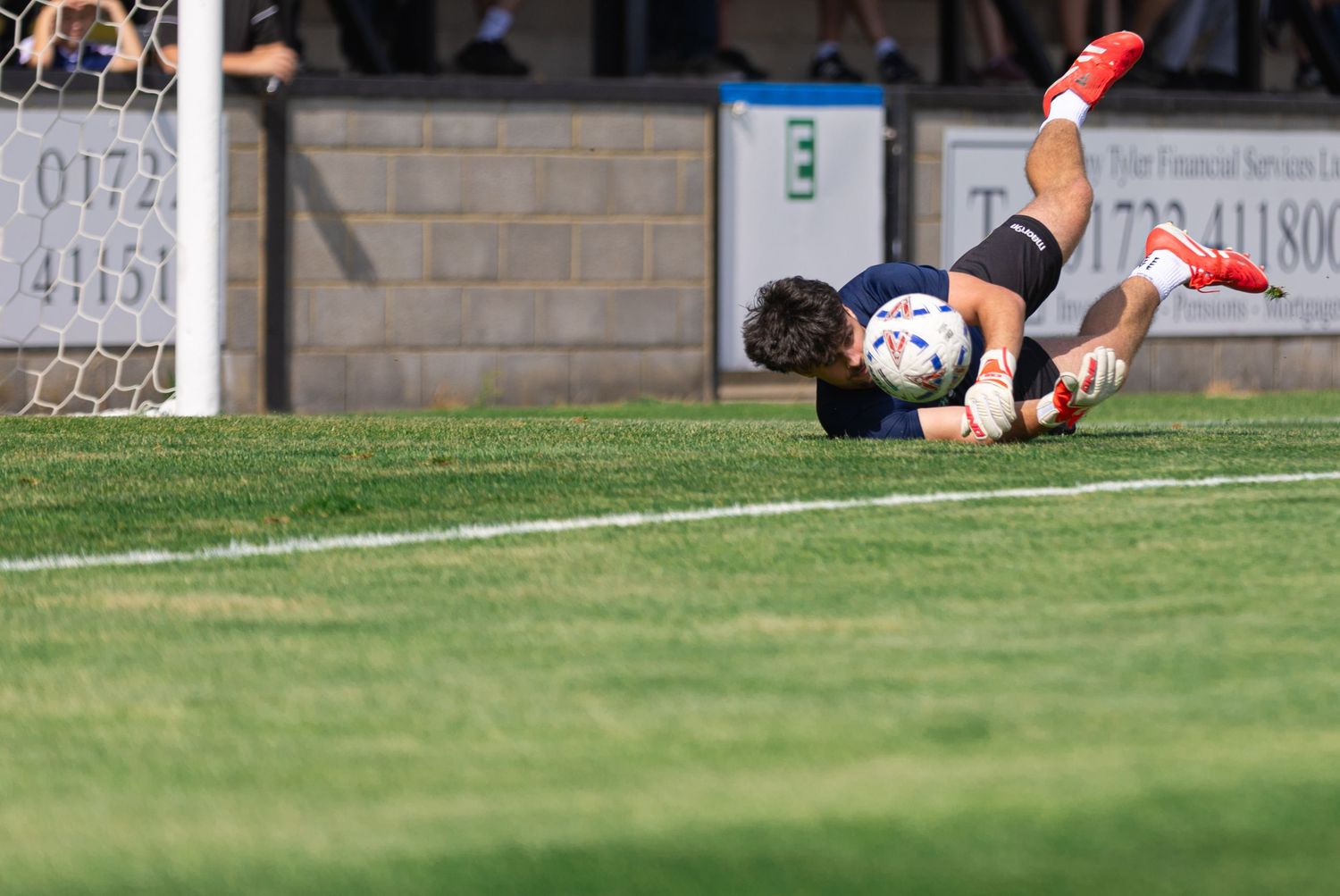 Rugby player diving to score a try on a green field during a sunny match.