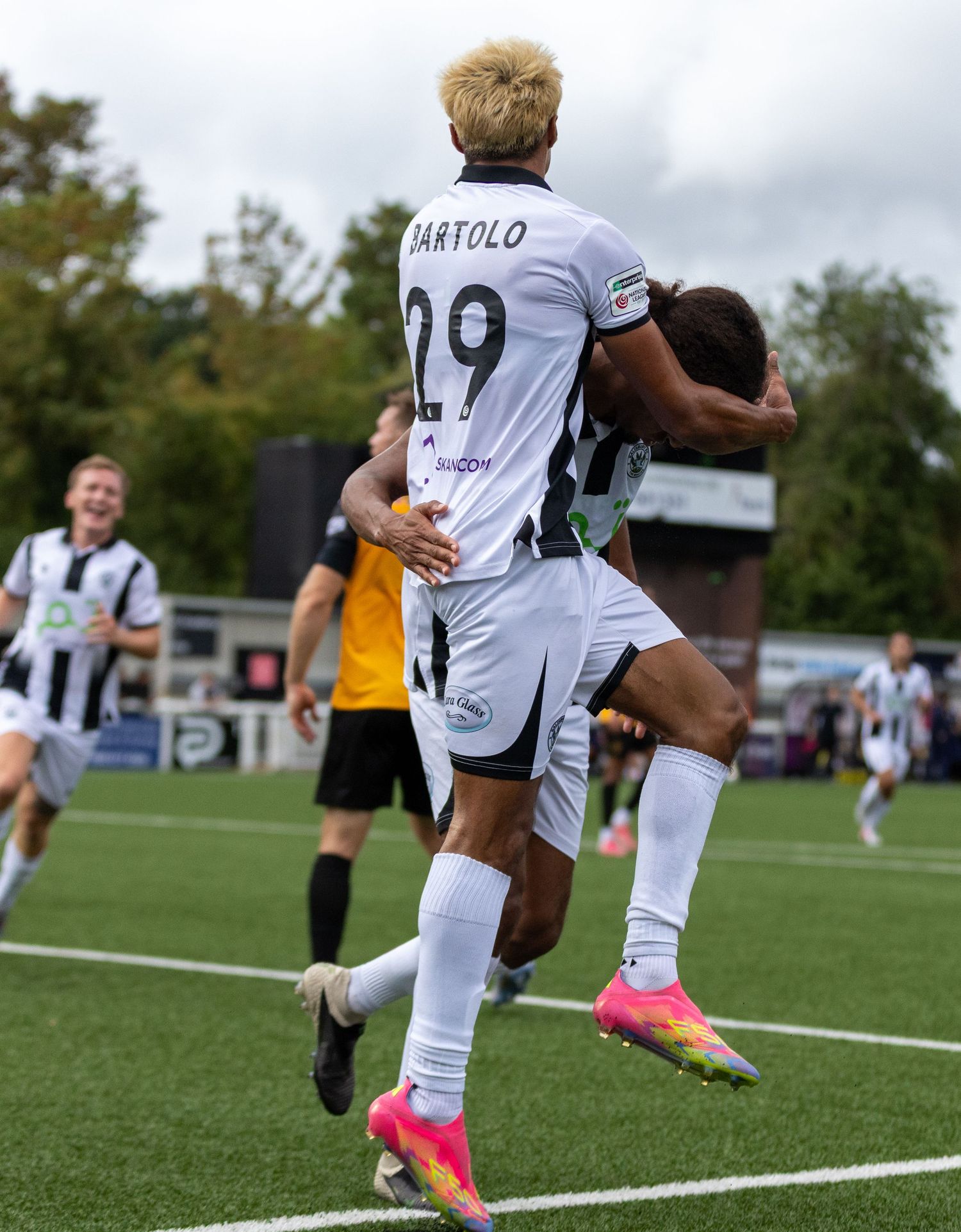 Soccer player Bartolo, number 29, celebrates a goal with a teammate during a match in white and black uniforms.