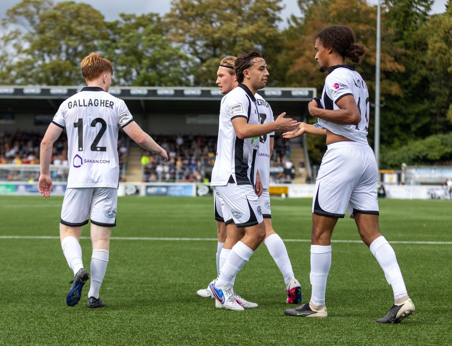 Football players in white uniforms celebrating a goal on a green pitch during a competitive match.