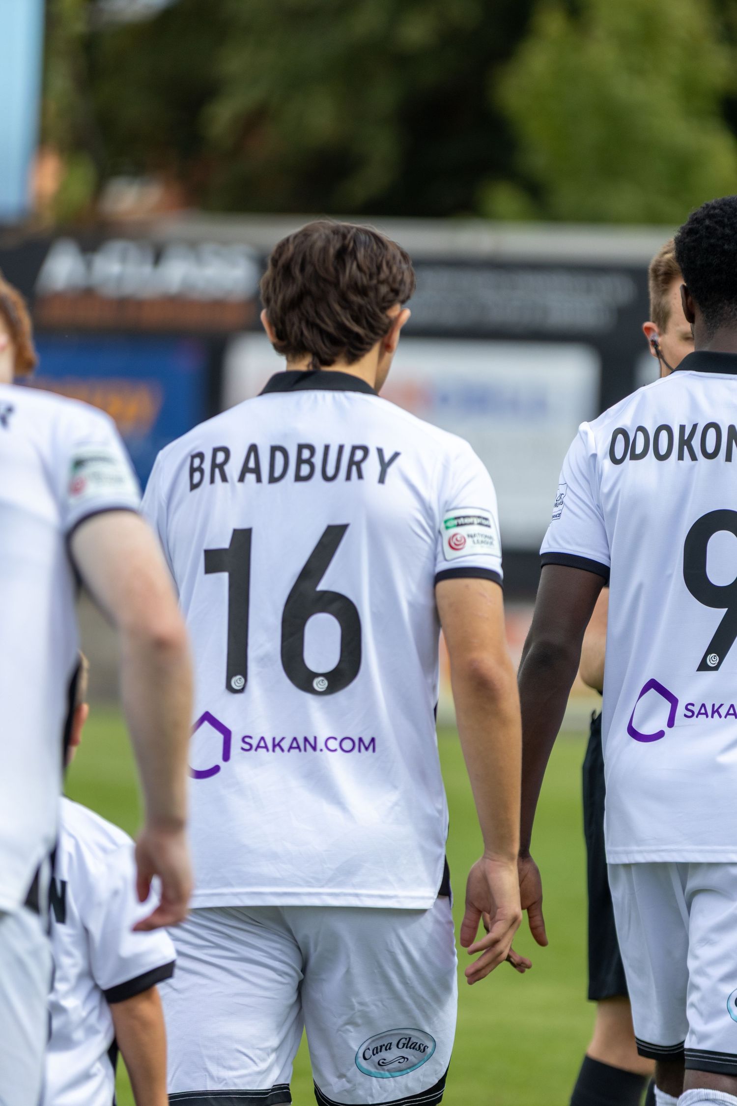 Footballer Bradbury number 16 walks alongside Odokon number 9 in white Sakan.com kits.