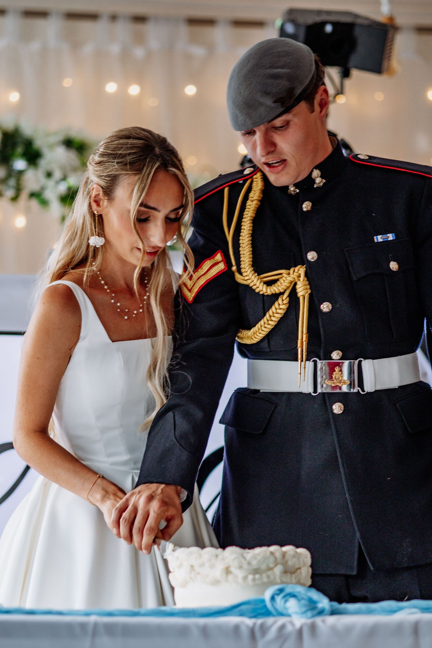 Bride in white gown and groom in military dress uniform cutting wedding cake.