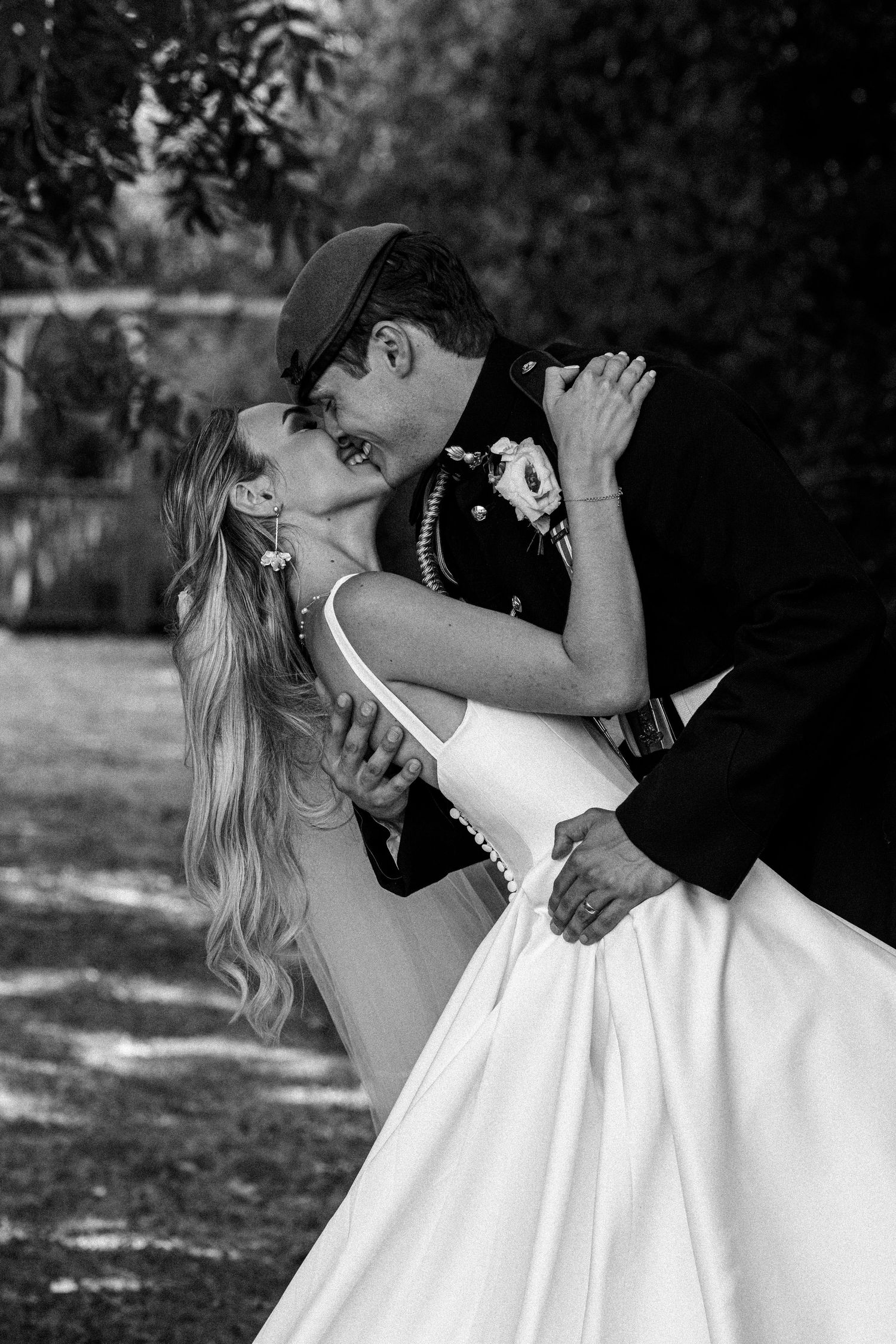Black and white wedding photo of bride and groom sharing a passionate dip kiss in garden setting.