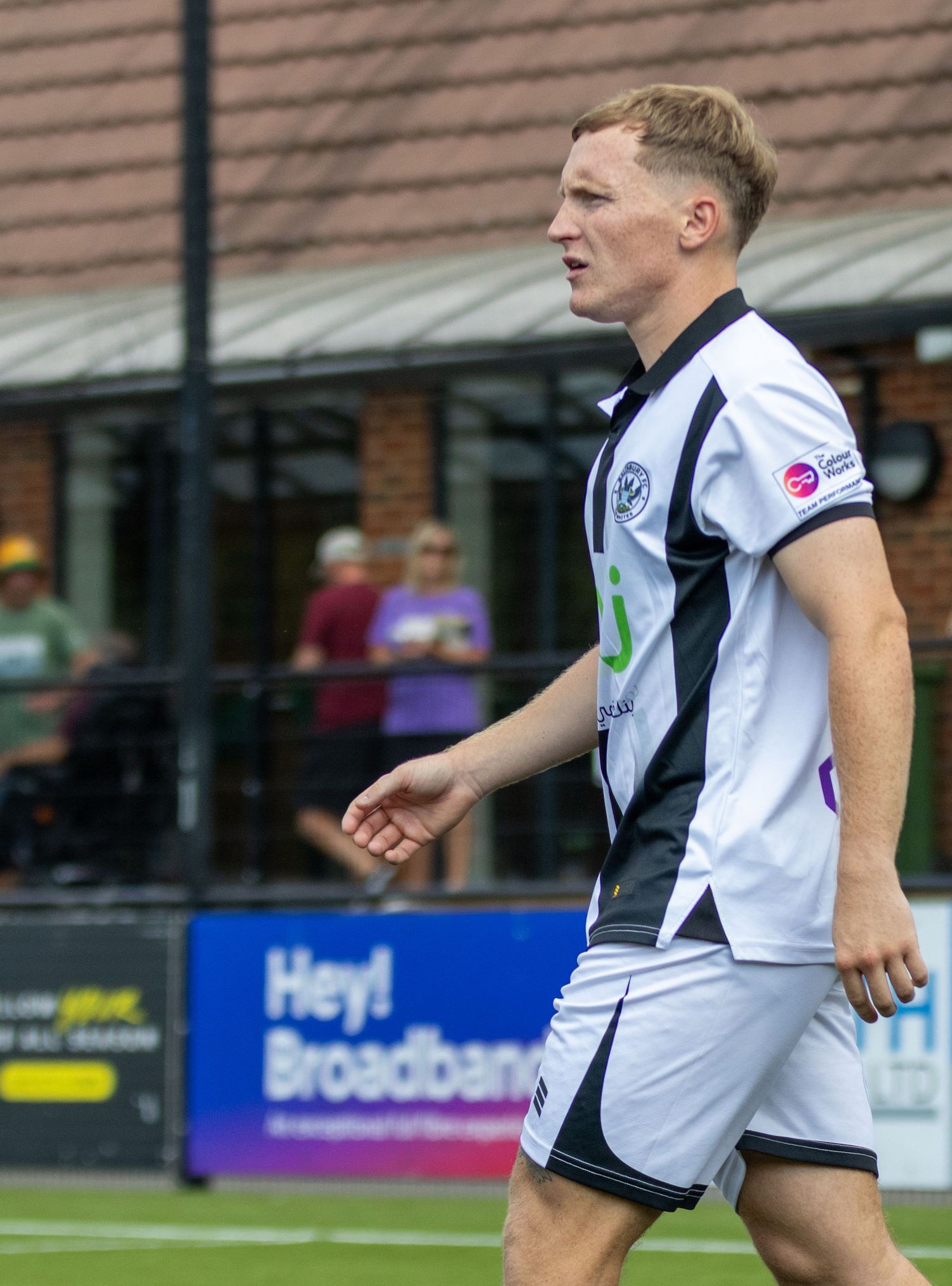 A blonde footballer in a black and white strip walks across the pitch during a non-league football match.