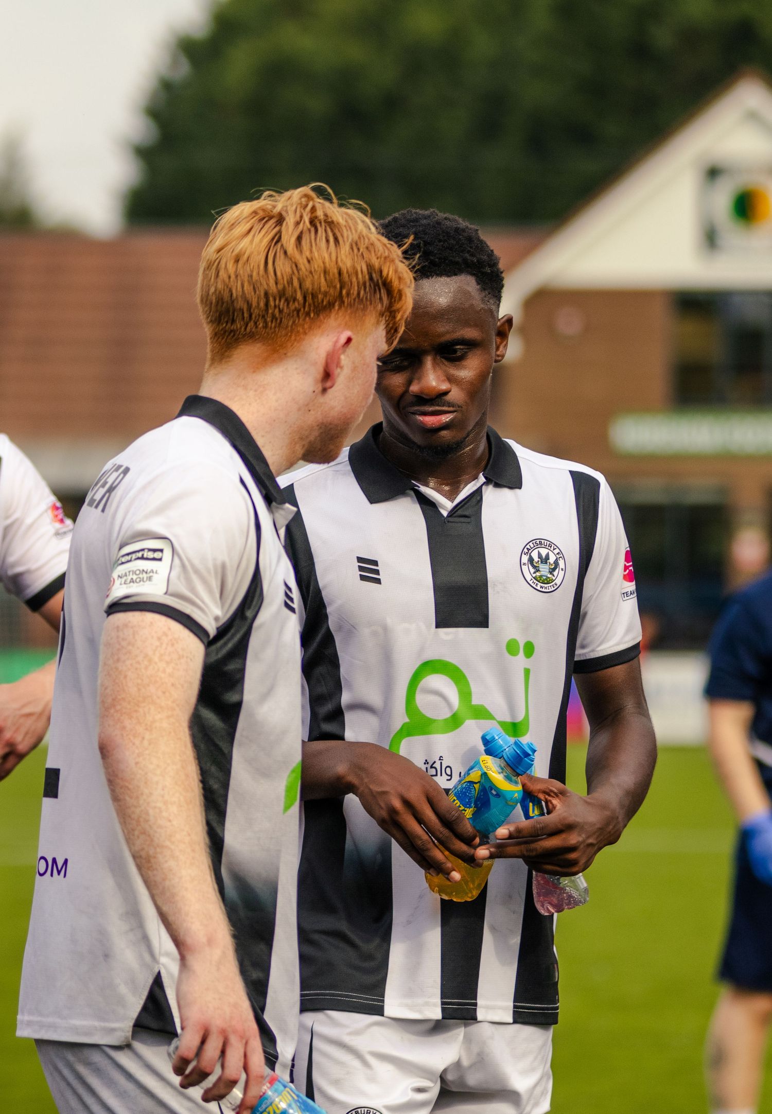 Two footballers in black and white striped kits share a conversation during a football match.
