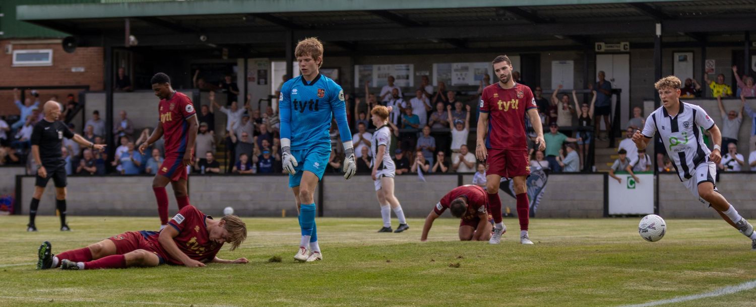 Football players react after a goal with some on the ground and others celebrating on the pitch.