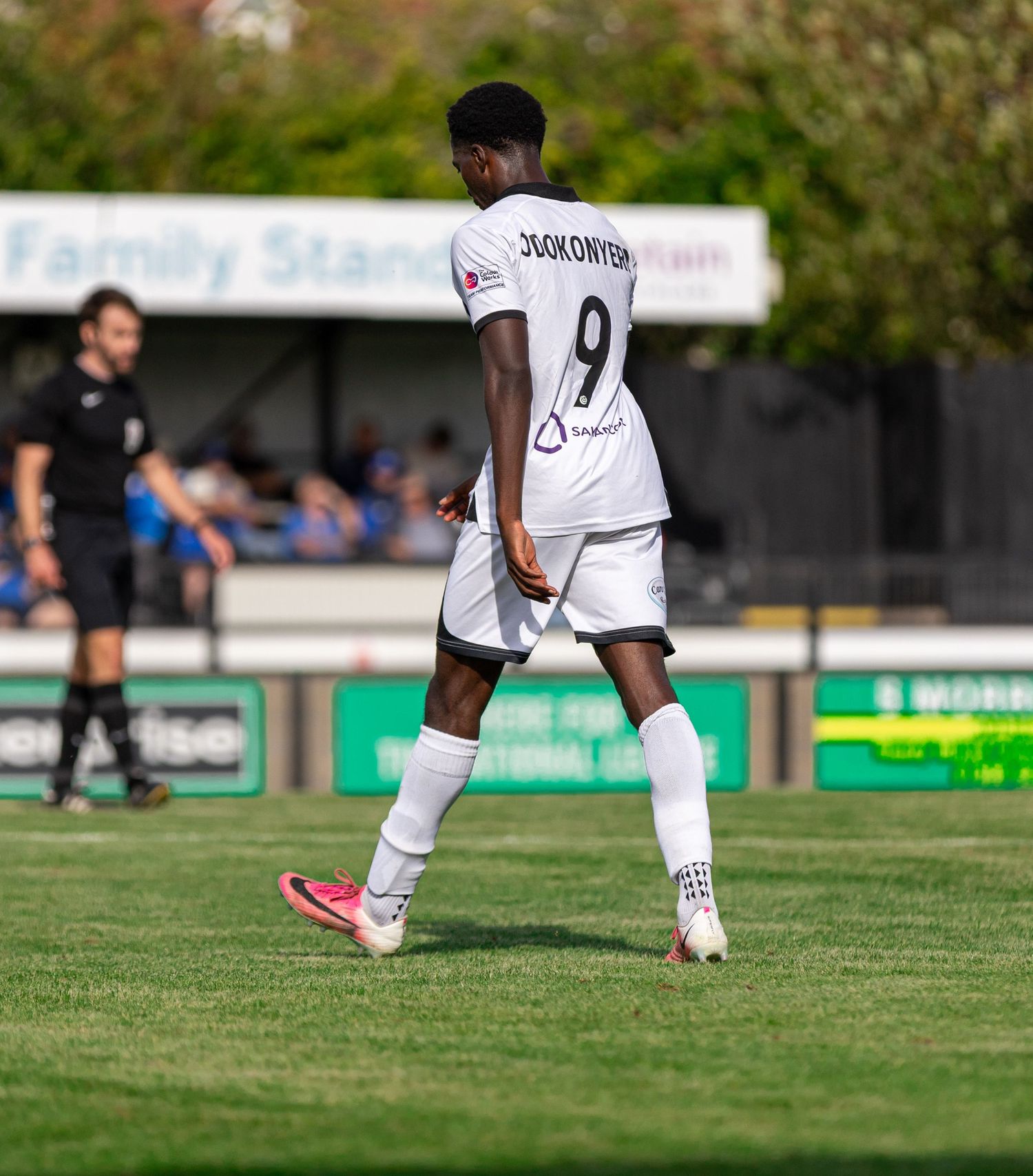 Football player Dookonyon wearing number 9 white jersey walks on green pitch during a sunny match day.