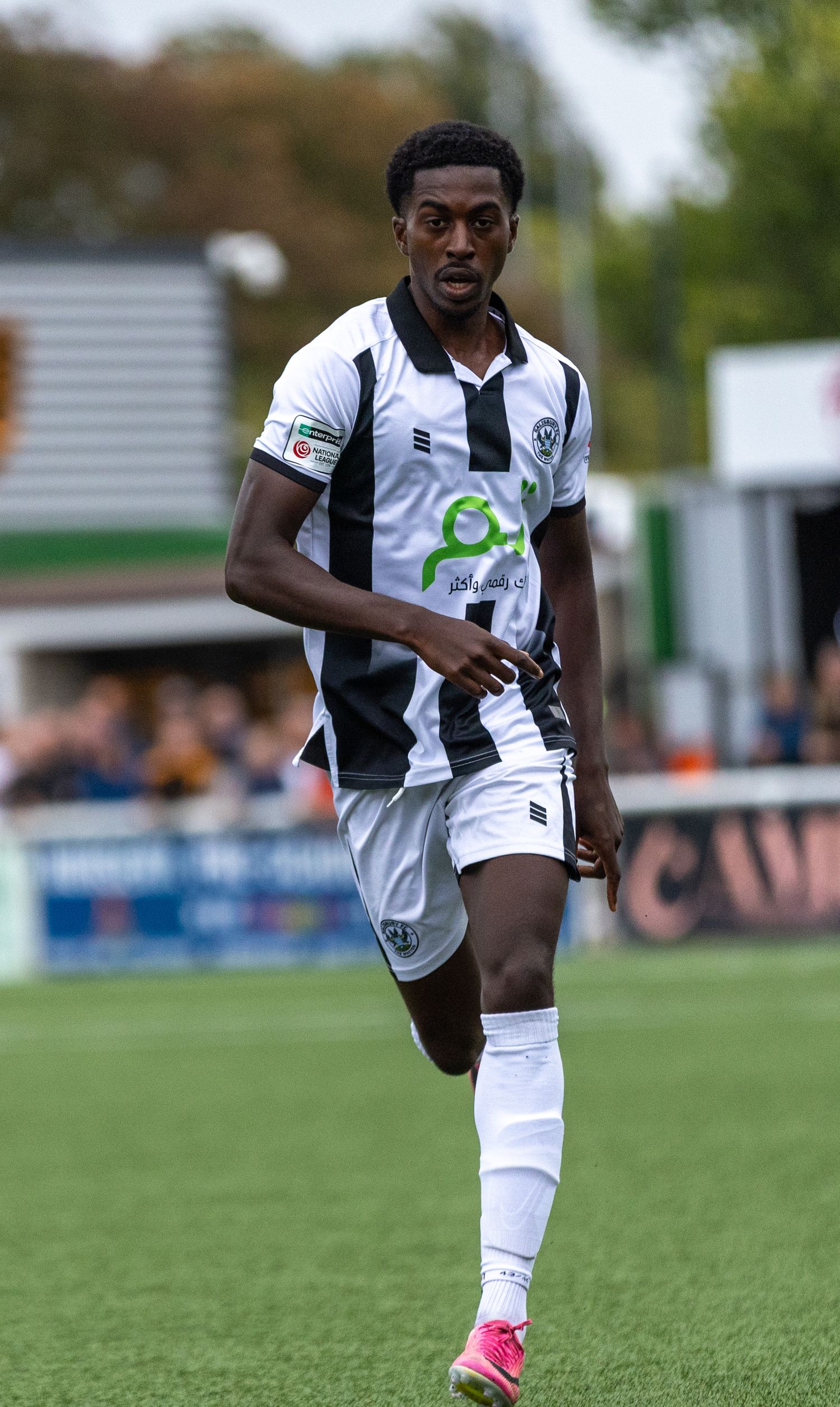A male soccer player in a black and white striped kit runs on a grass pitch during a football match.