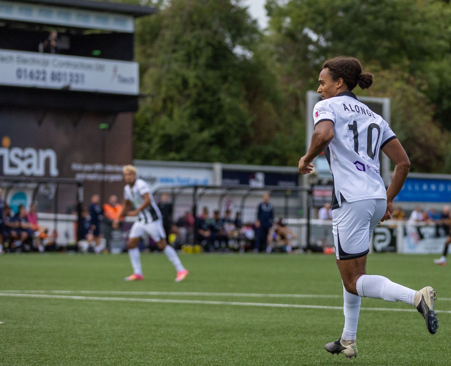 Female soccer player wearing number 10 jersey runs on green pitch during outdoor football match at a local stadium.