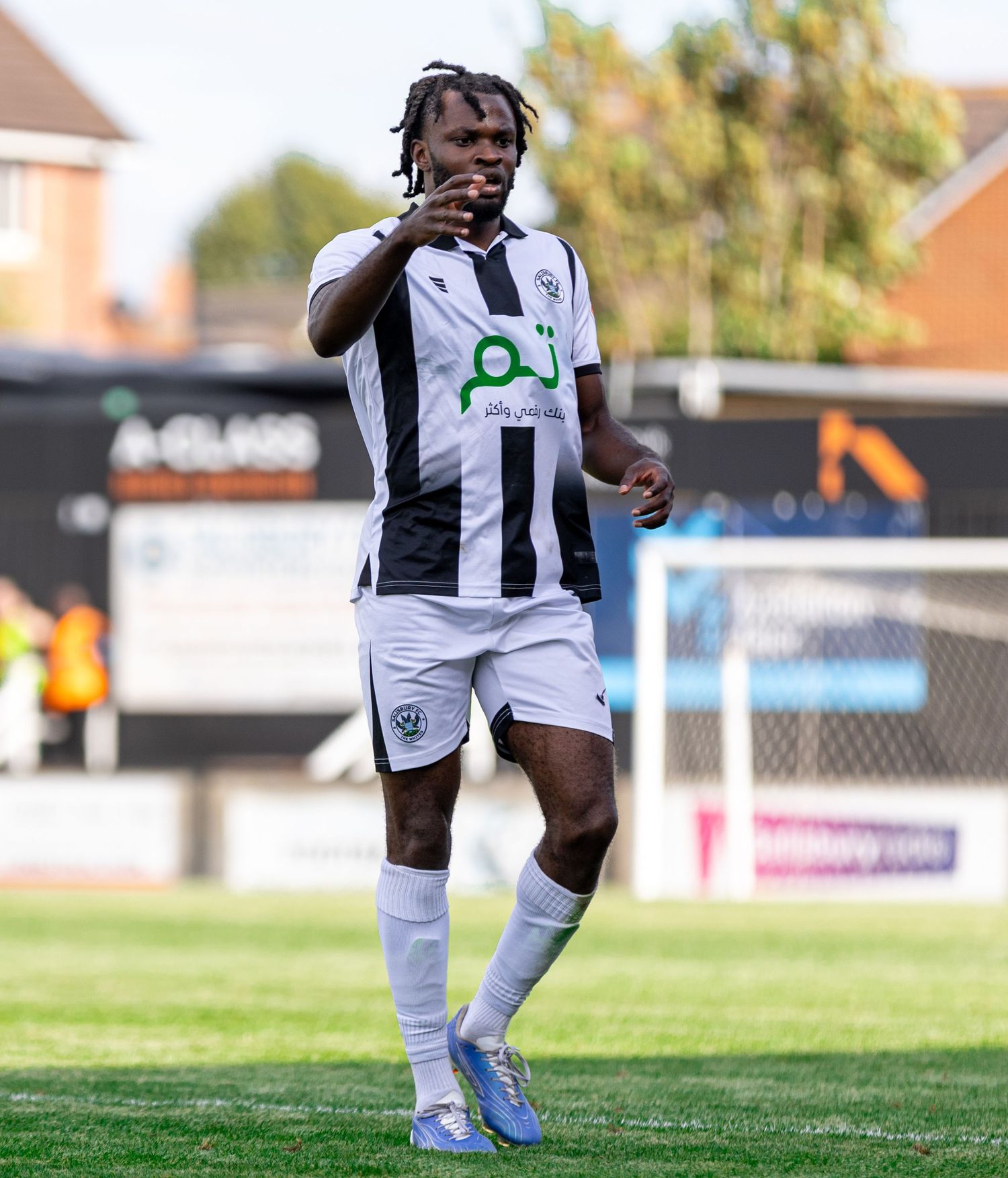 Football player in black and white striped kit celebrating on pitch during a sunny match day.