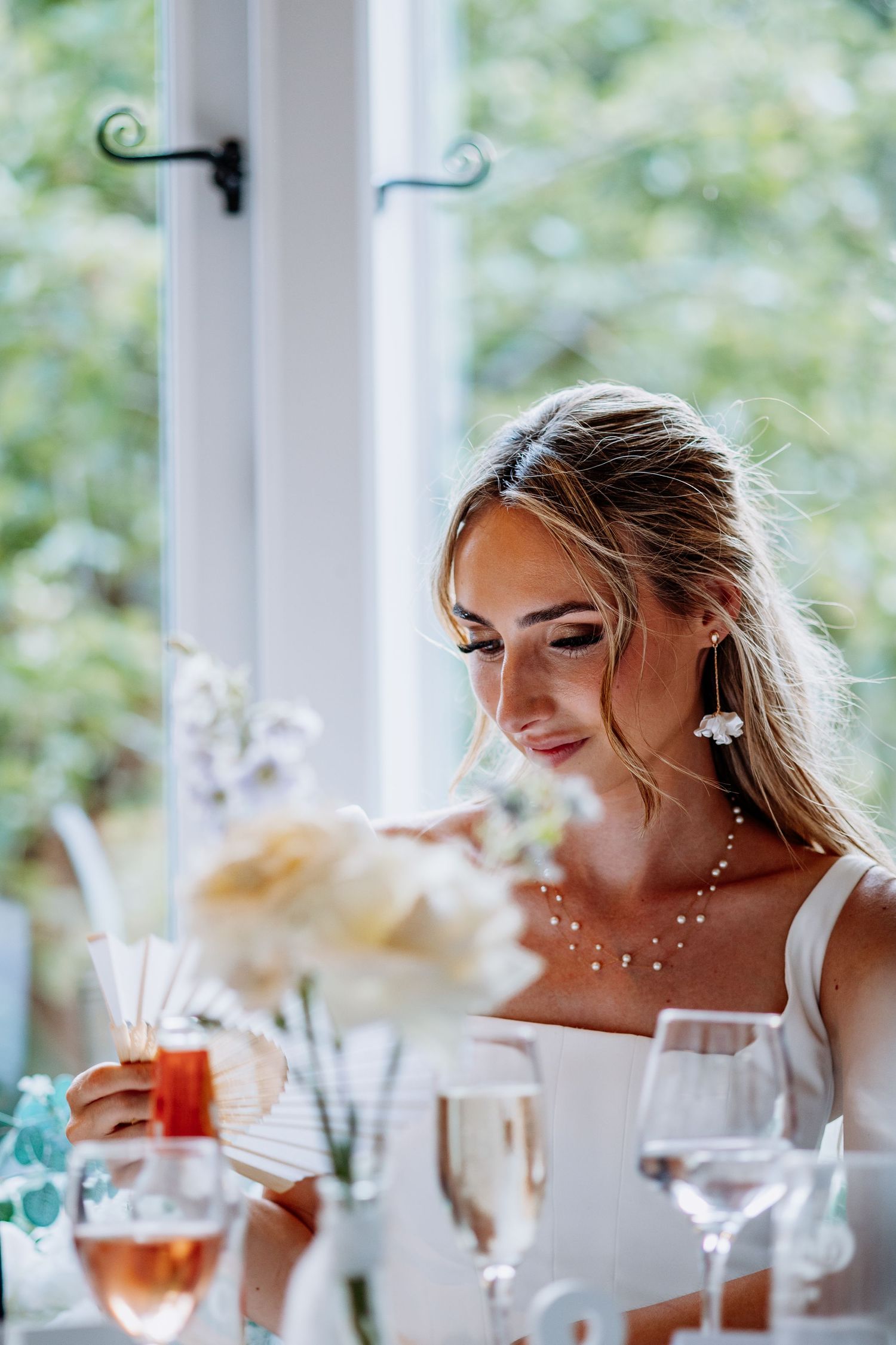 Elegant bride in white dress sitting at wedding reception table with champagne and floral centerpieces.