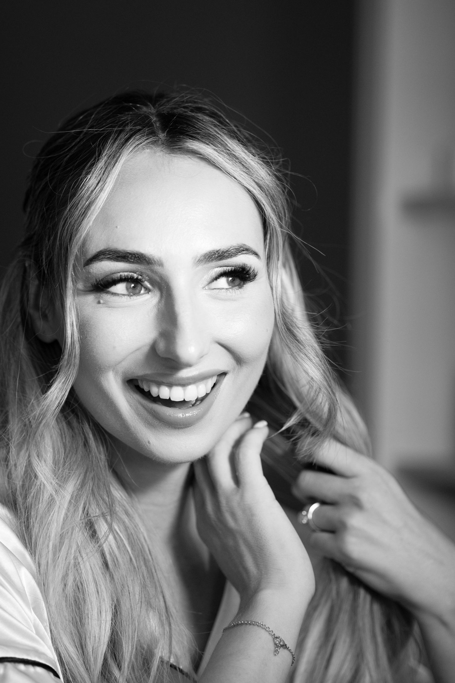 Black and white portrait of a smiling blonde woman with glamorous makeup touching her hair.