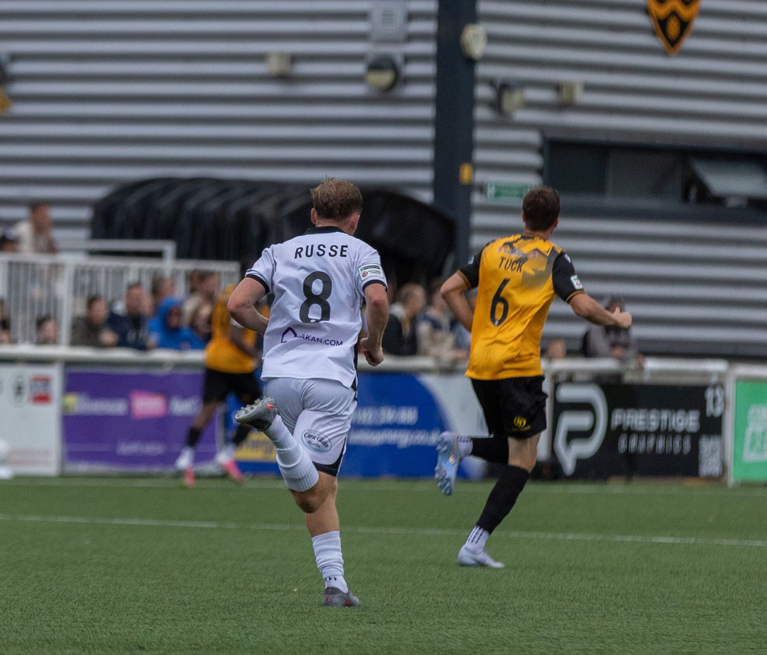 Soccer players in action, player number 8 in white jersey and player number 6 in yellow and black kit on green pitch.