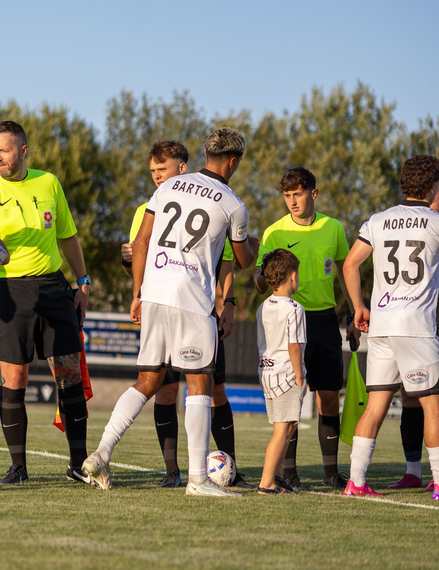 Players Bartolo number 29 and Morgan number 33 line up with a referee and mascot before a football match.