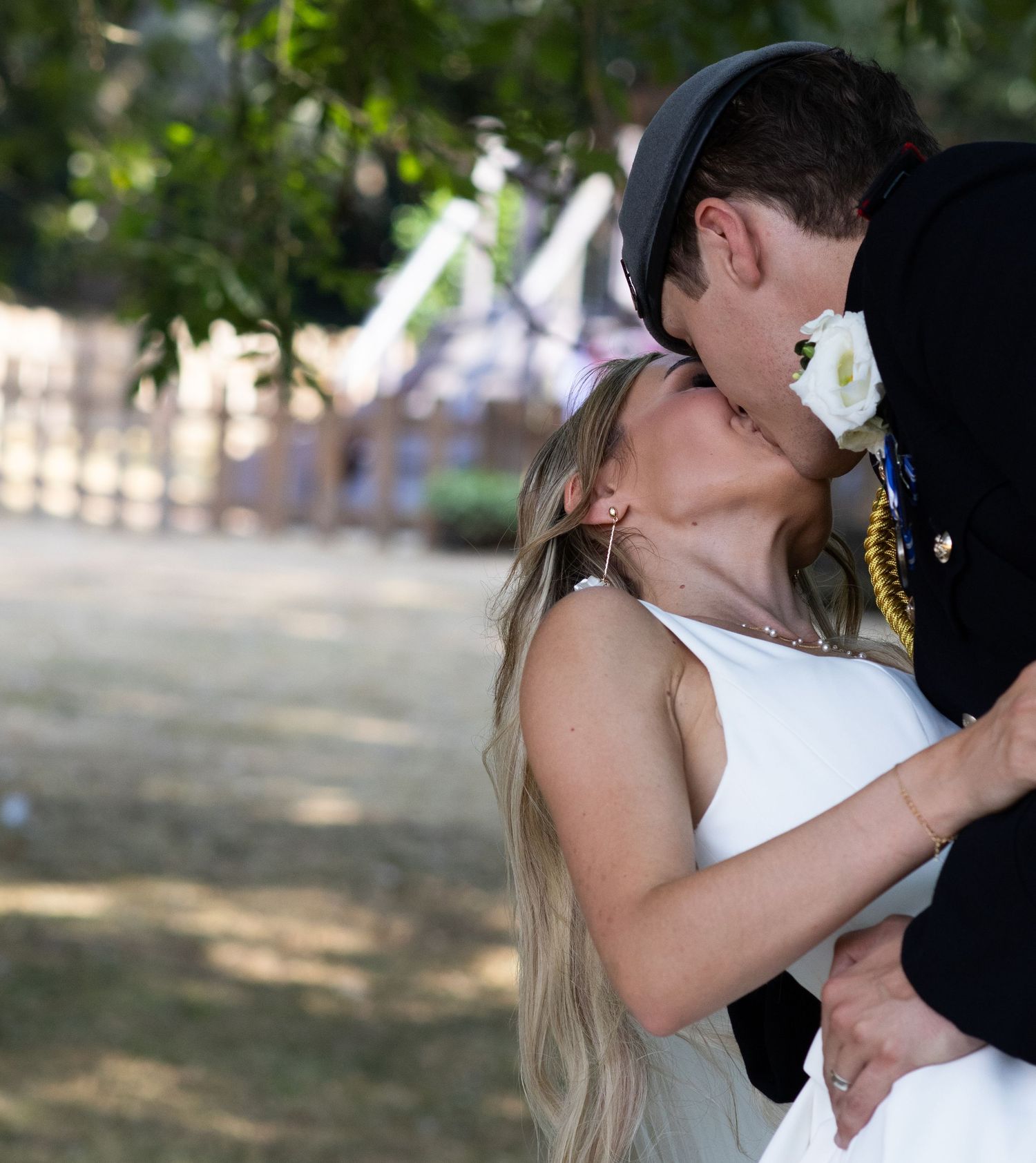 Bride and groom share a passionate kiss under trees at outdoor wedding.