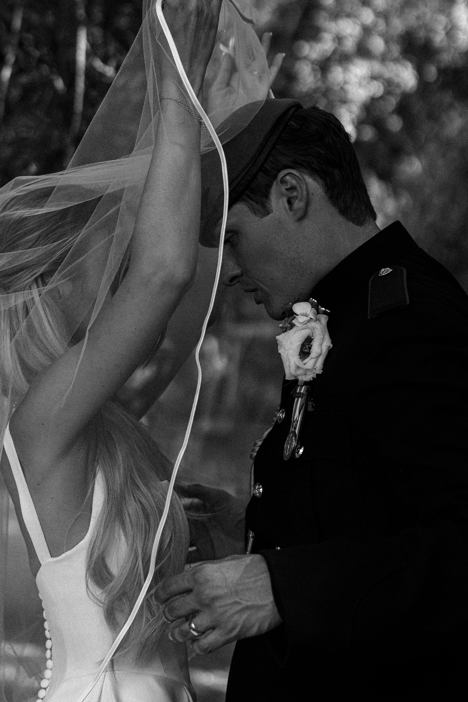 Black and white photo of bride and groom in military uniform sharing an intimate moment under a veil.