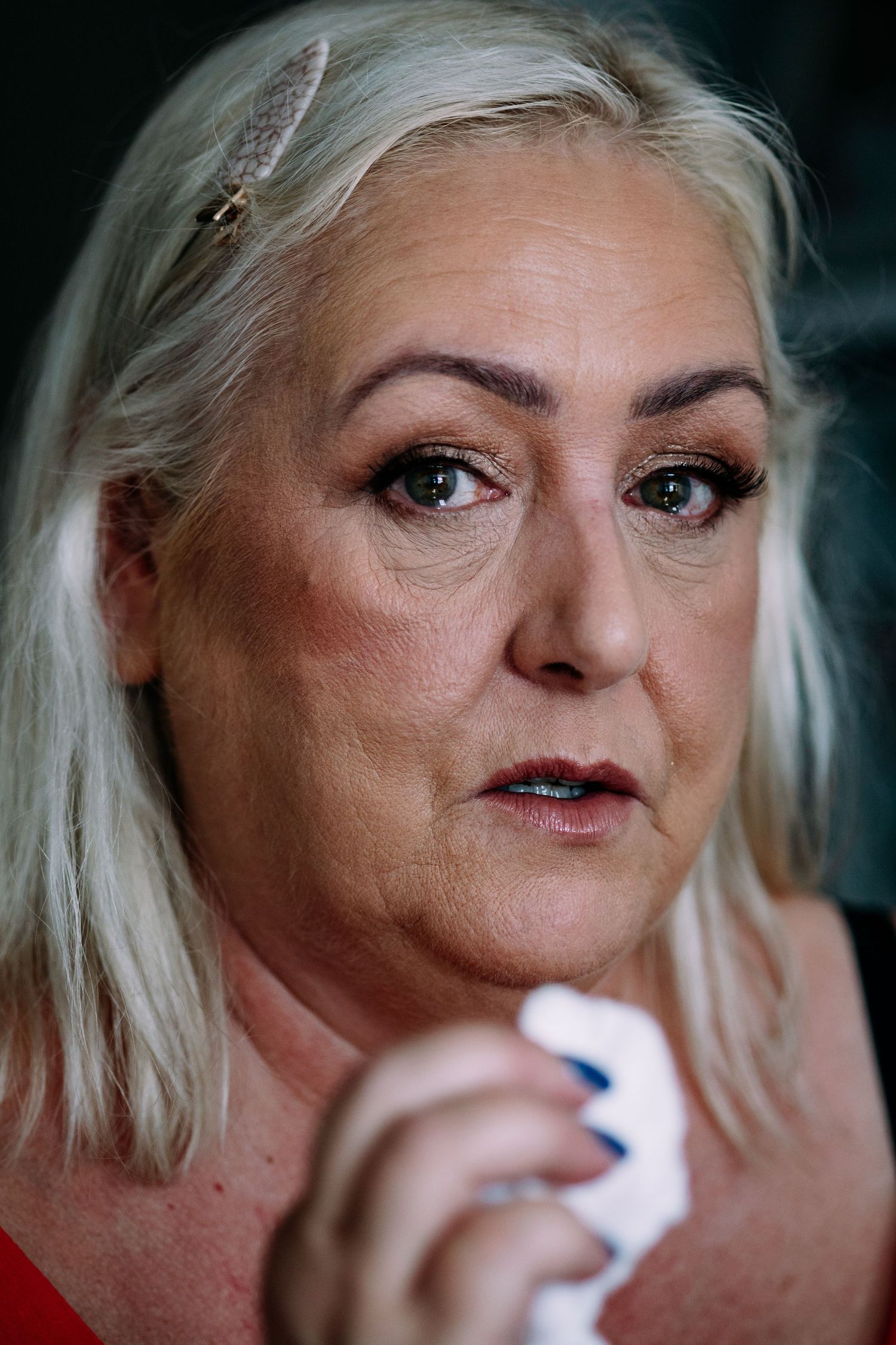 Emotional older blonde woman with hair clip holding tissue during wedding preparations.