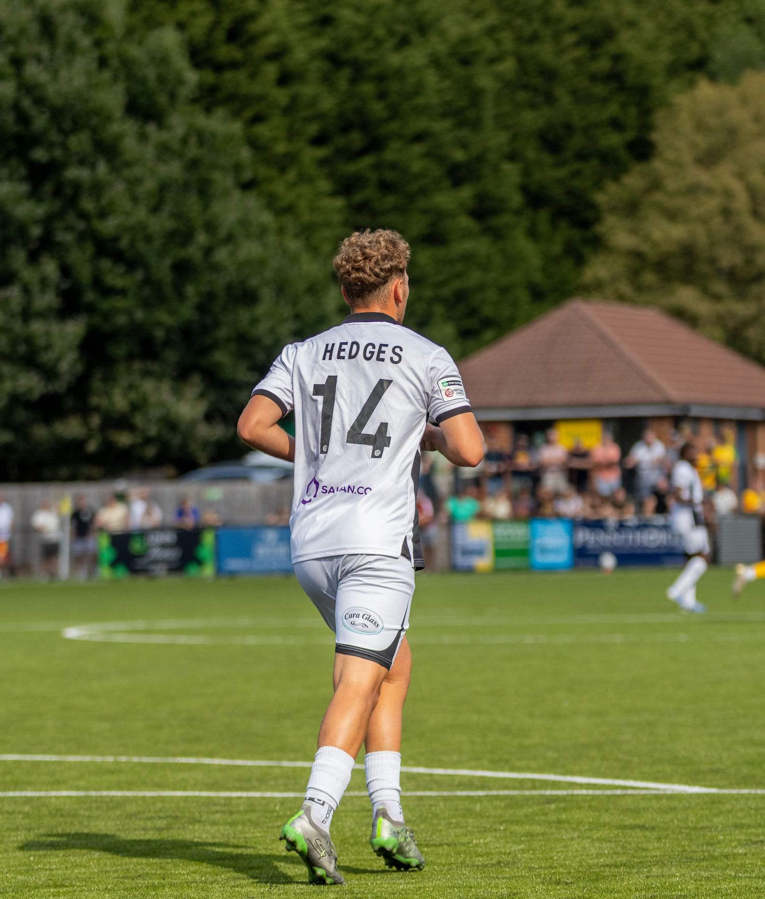 Footballer Hedges wearing number 14 white away kit walks on green pitch during a sunny outdoor match.