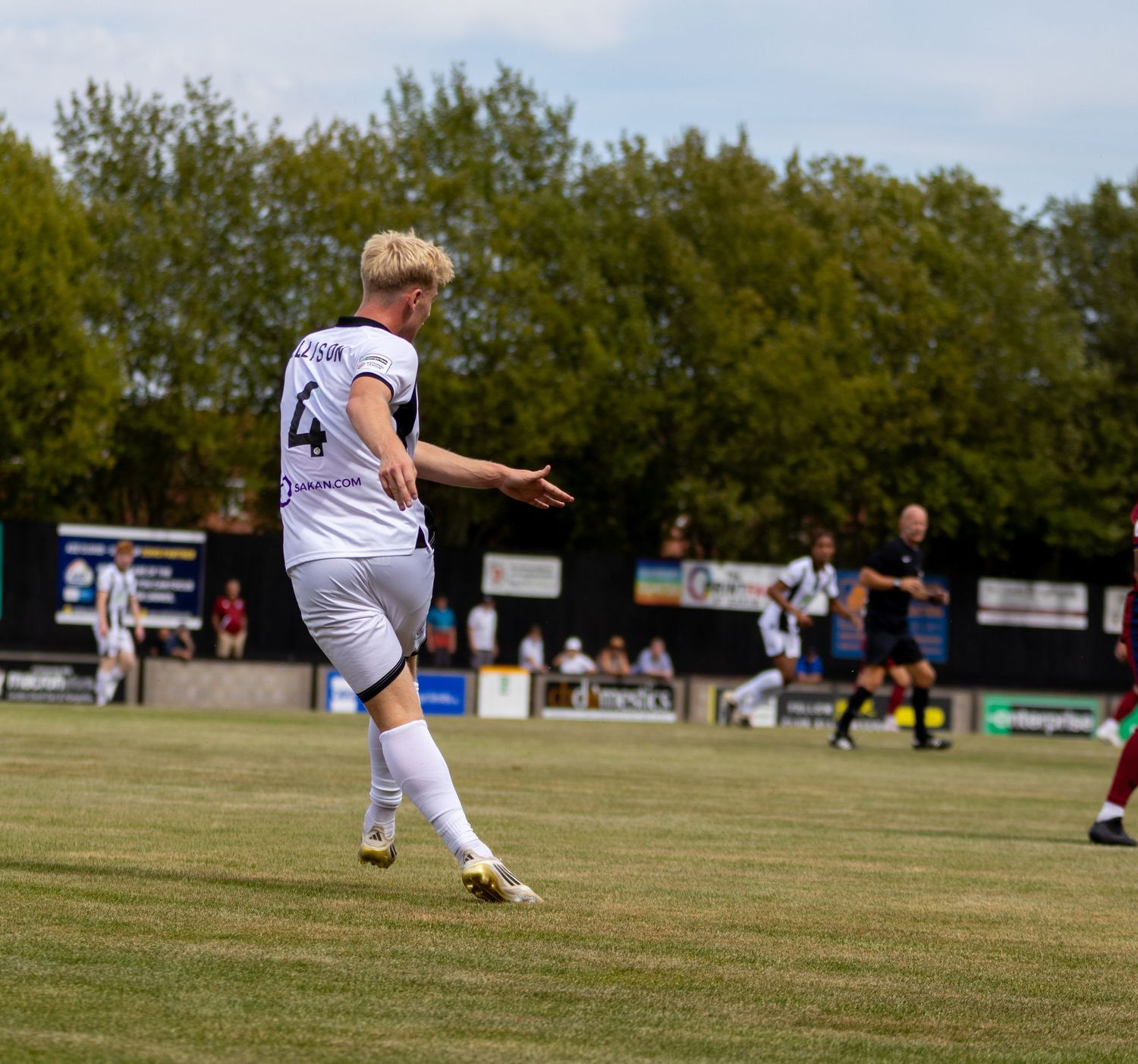 Football player number 4 in white kit kicks ball during outdoor match on sunny day.