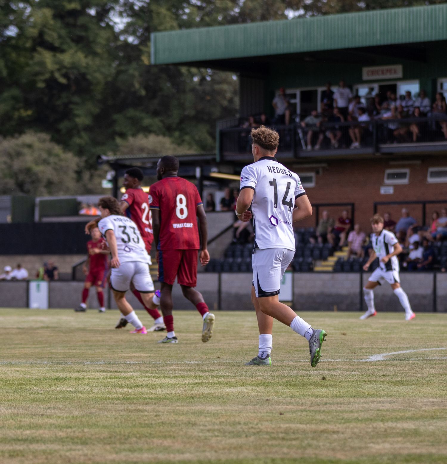Salisbury FC player number 14 jogs during a non-league match with supporters in the background.