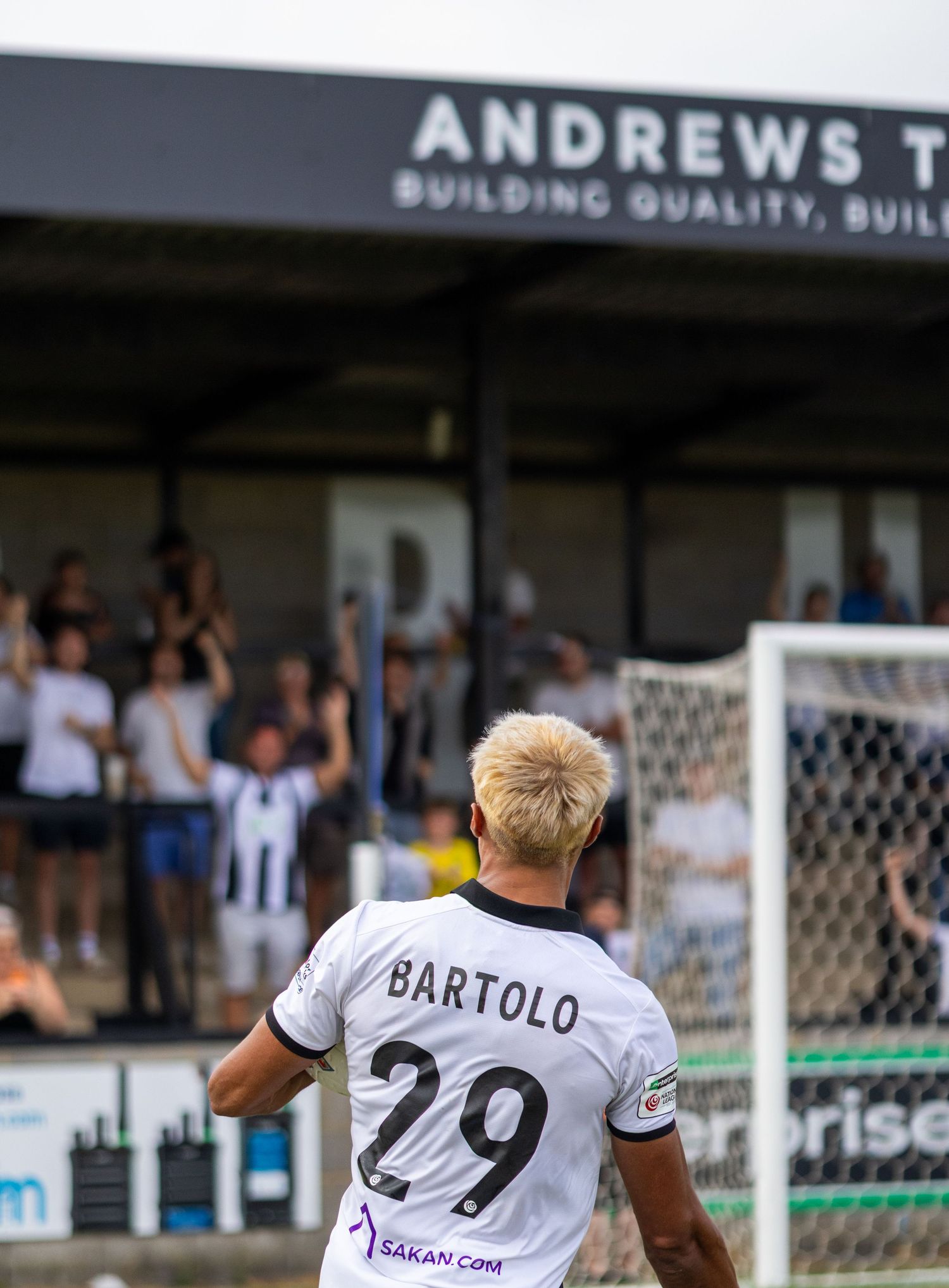 Football player Bartolo number 29 celebrates goal as fans cheer behind Andrews T building.