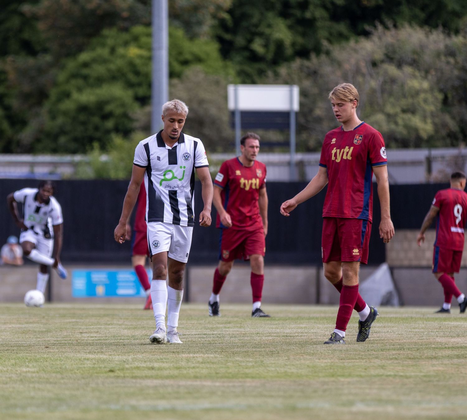 Two footballers in contrasting black-white and red kits walk on the pitch during a competitive match.