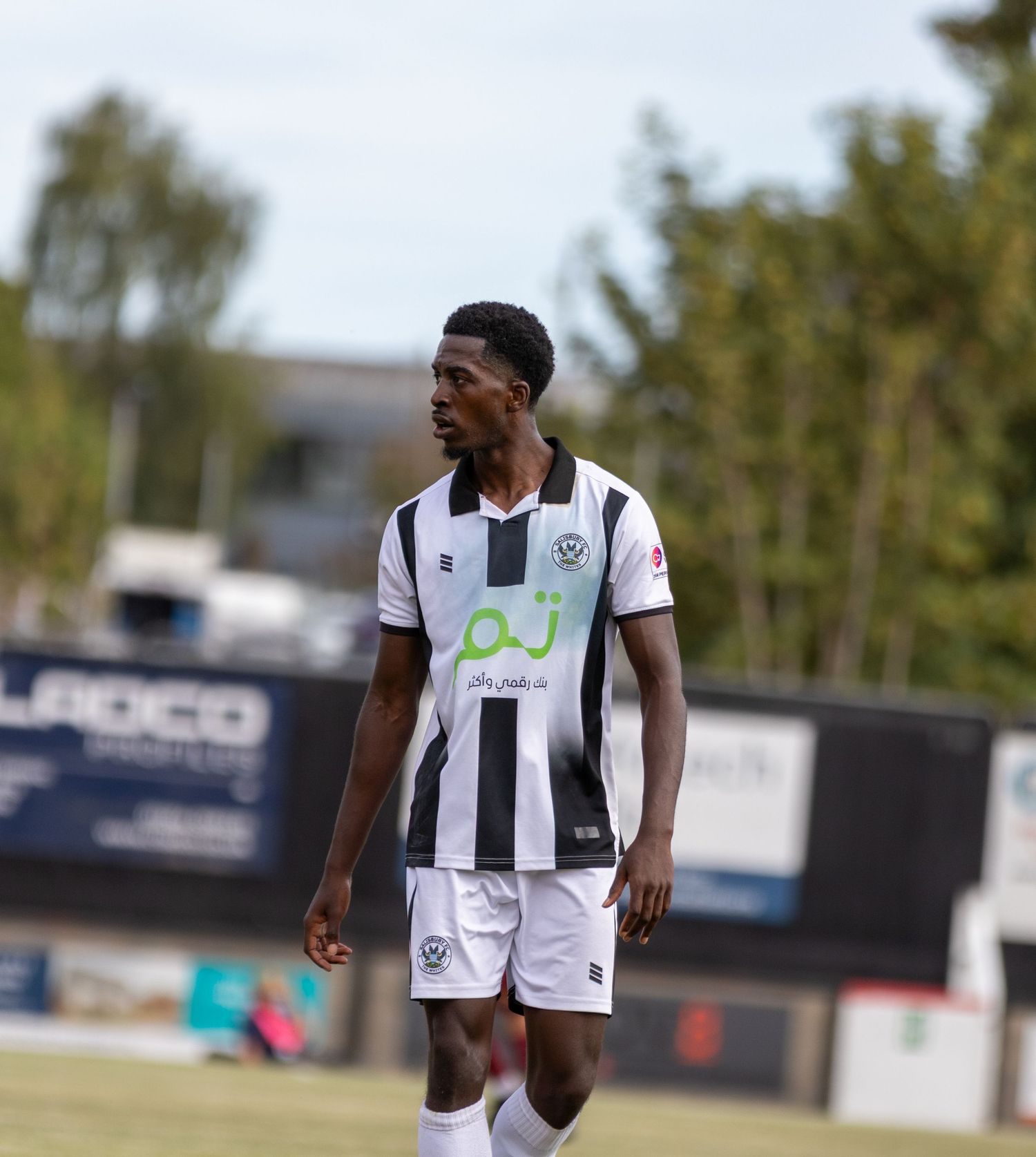 Close-up of a football player in black and white striped kit walking on the pitch during a match.