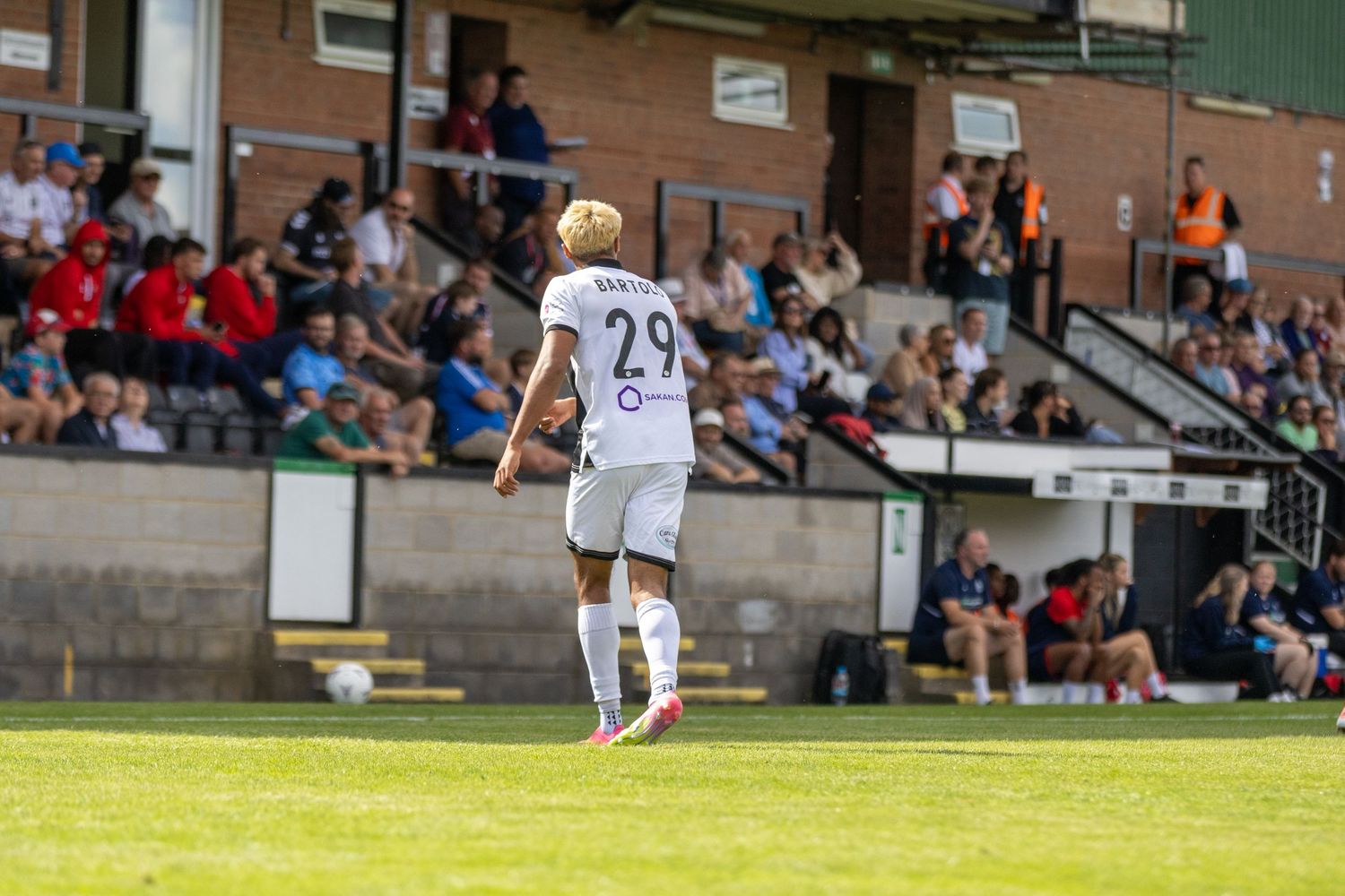 Soccer player number 29 in white kit walks on the pitch during a sunny football match.