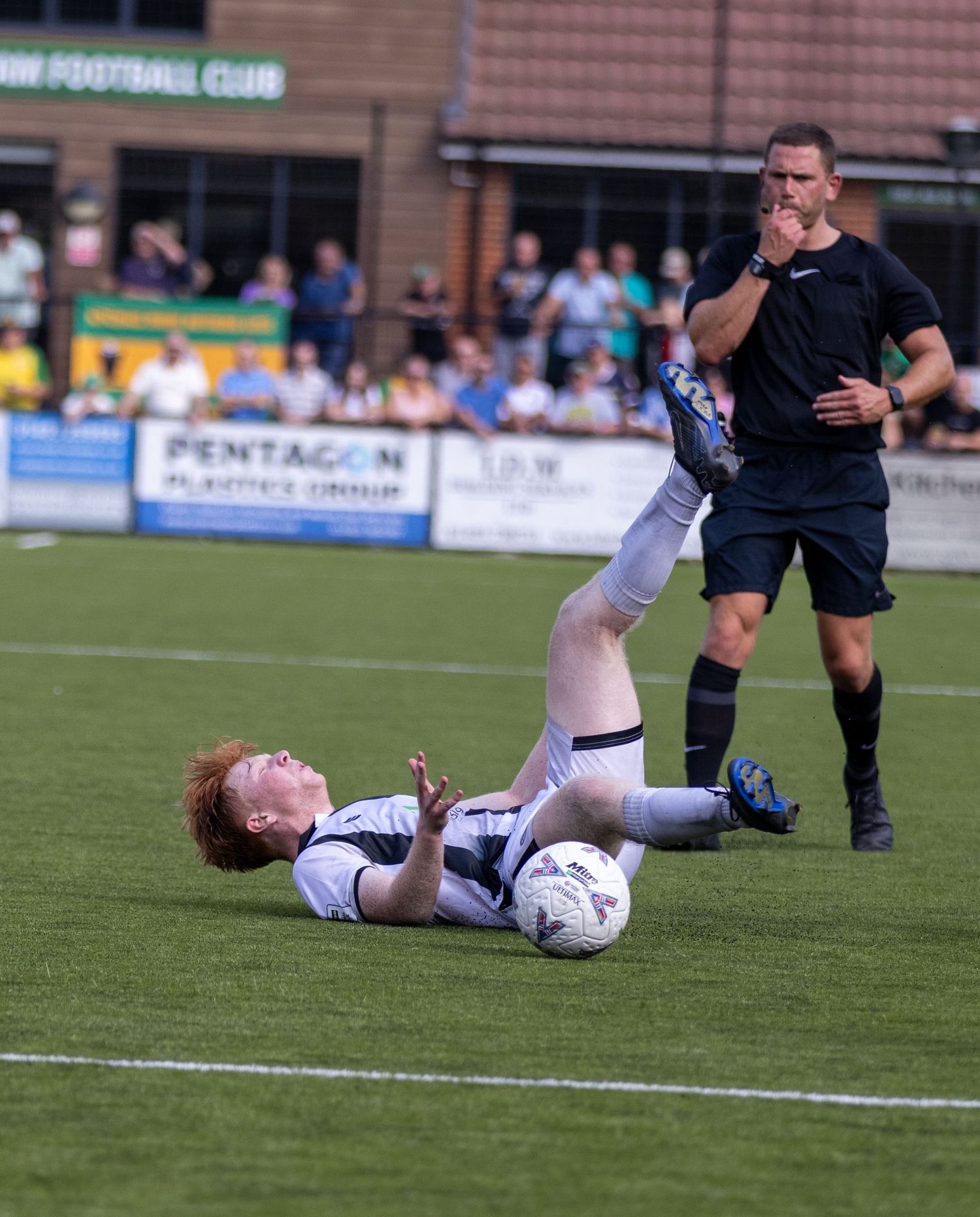 Soccer player slides on grass to control ball as referee watches during competitive match.
