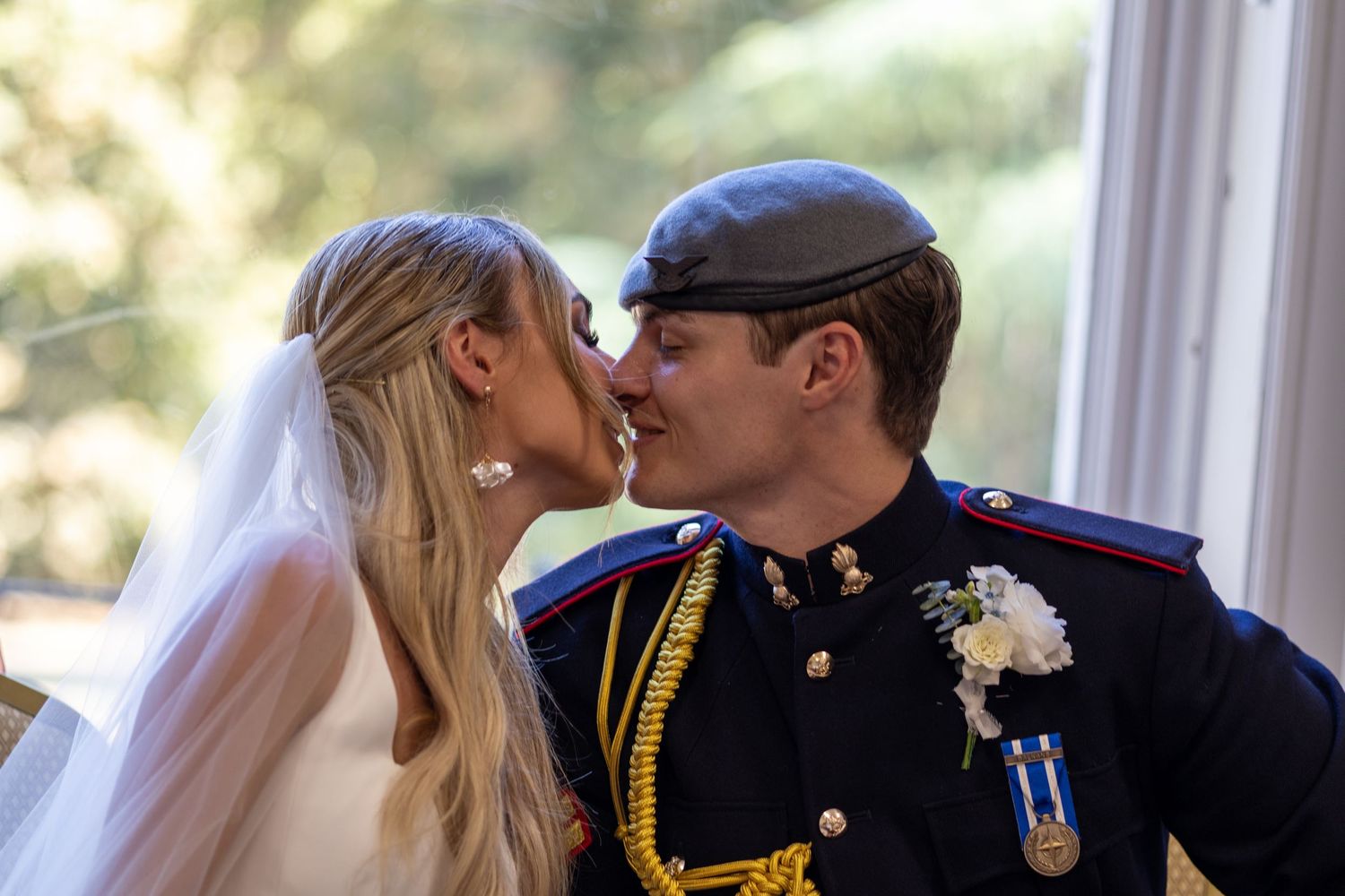 Bride and groom kissing, groom wearing military dress uniform with medals.