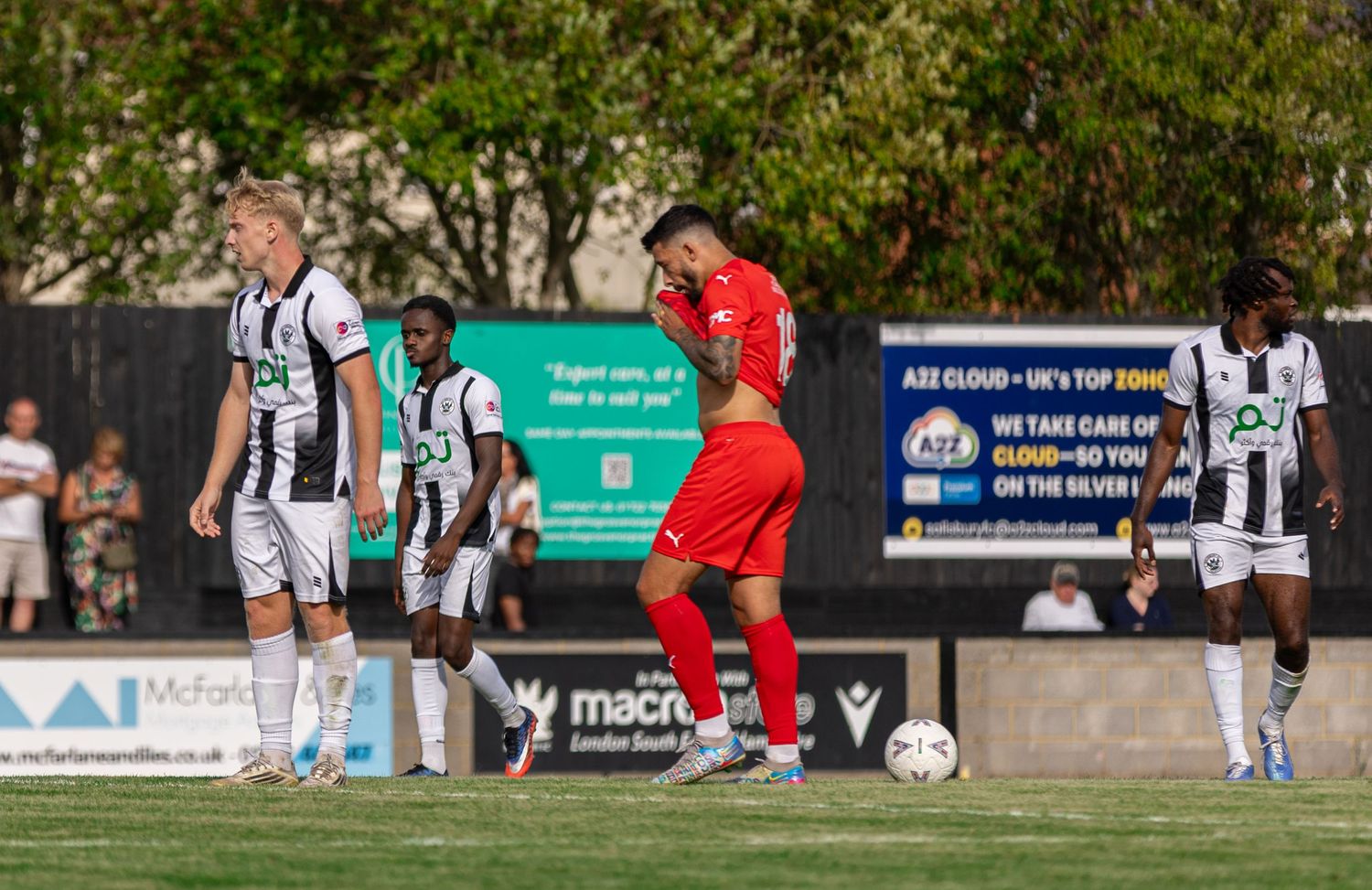 Football players in black-and-white and red kits during an outdoor match on a sunny day.