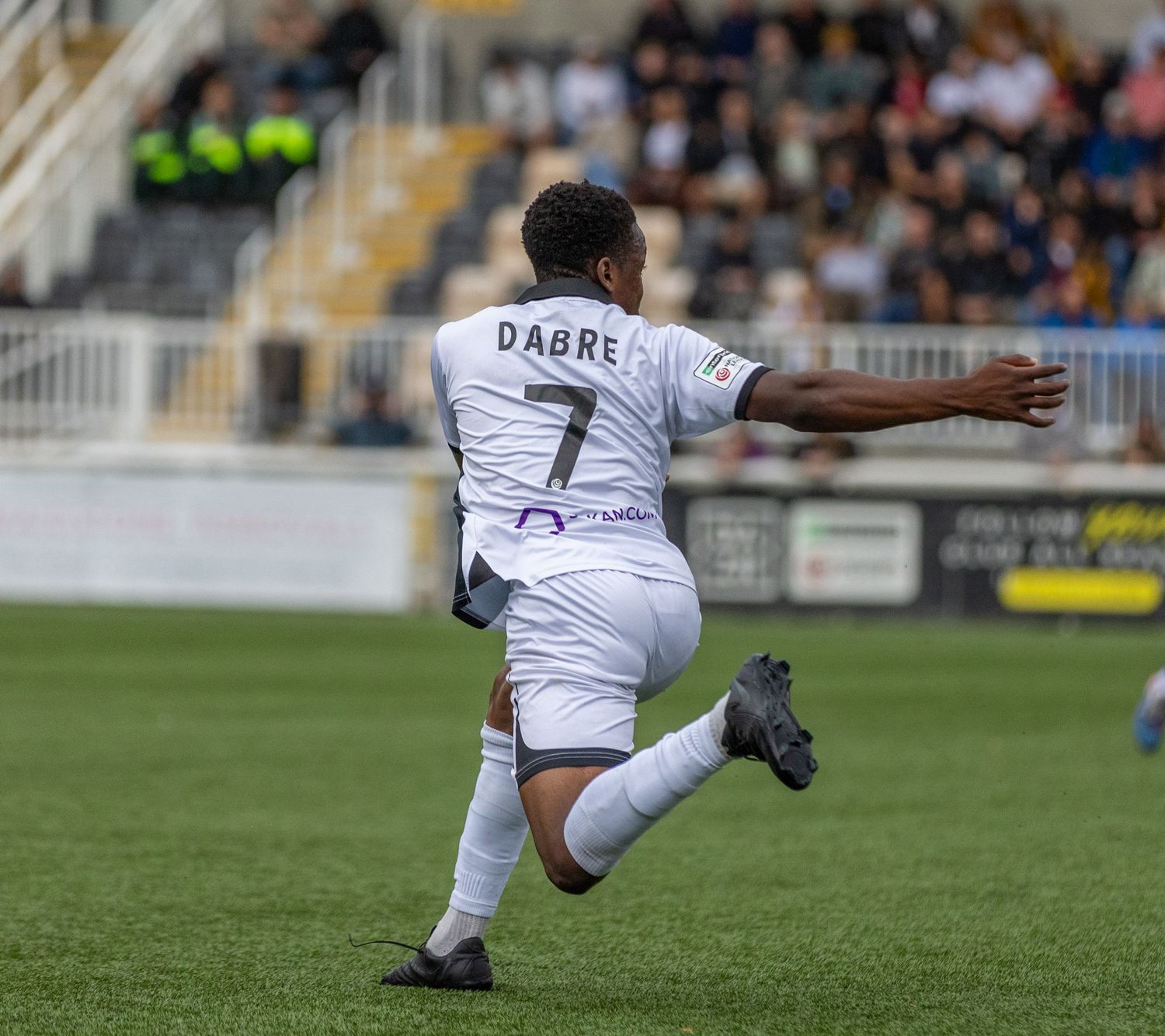 Soccer player Dabre wearing number 7 white jersey mid-kick during a professional football match at a stadium.