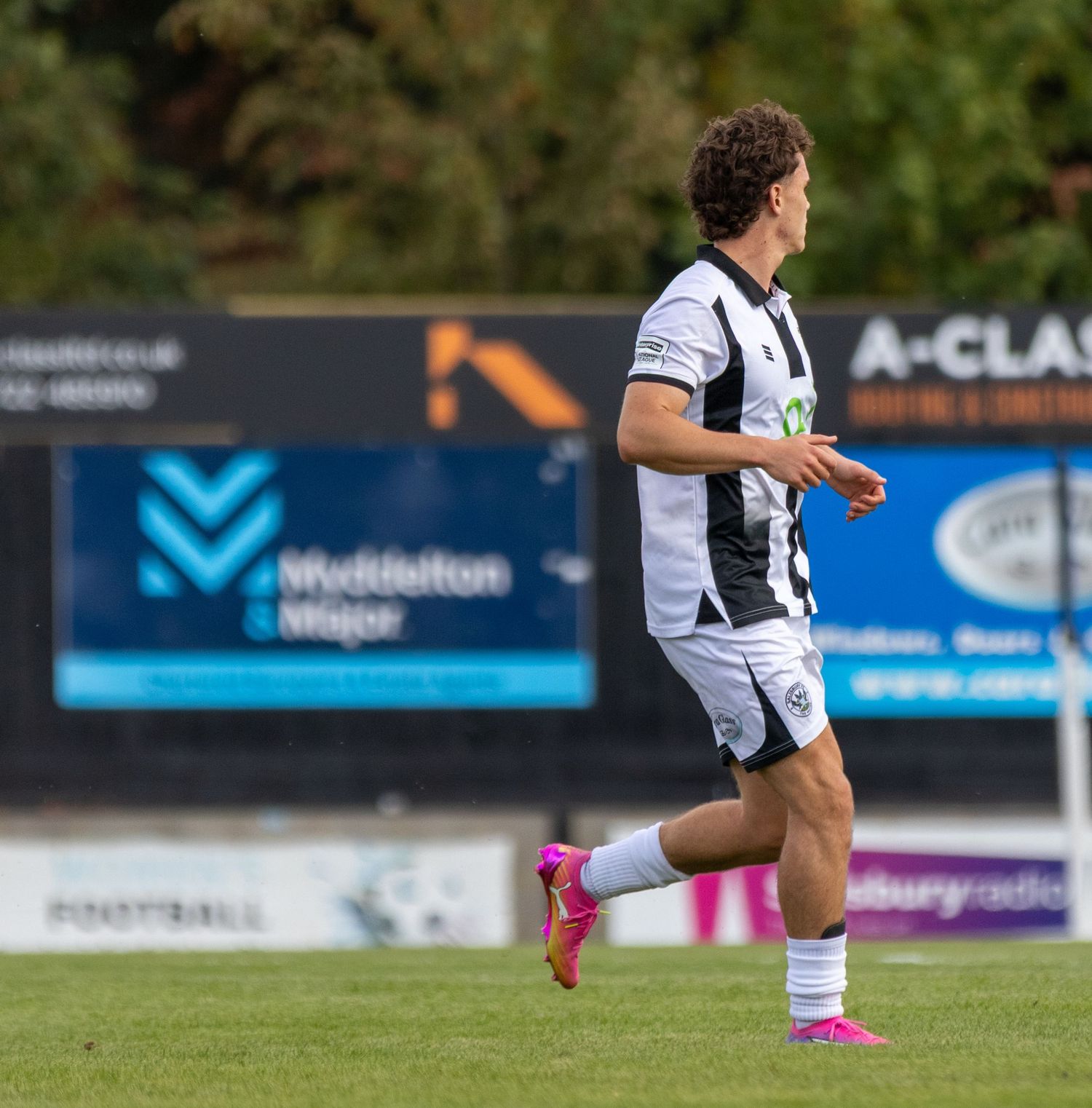 Soccer player in black and white kit running on pitch with advertising boards in background.