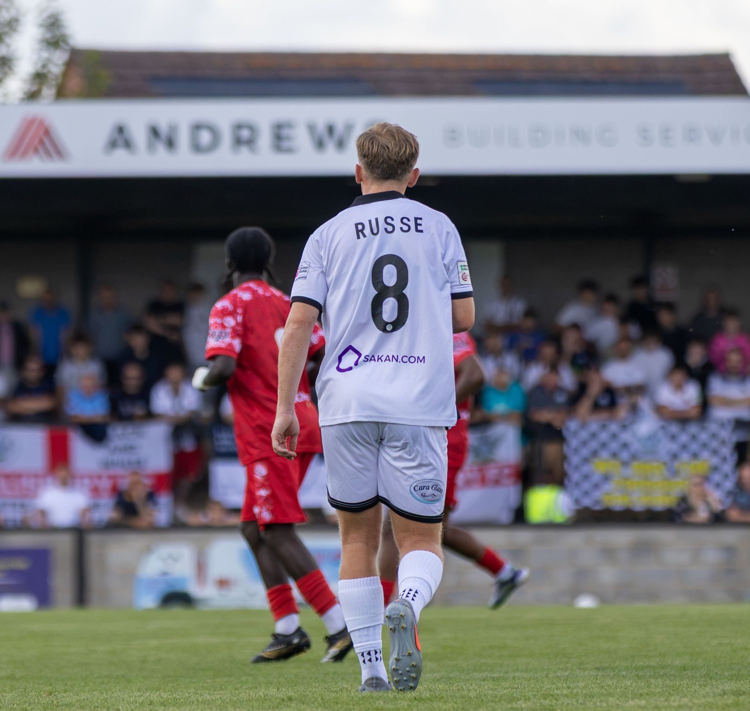 Football player Russe number 8 in white kit walks toward crowd at Andrews Building Services stadium.