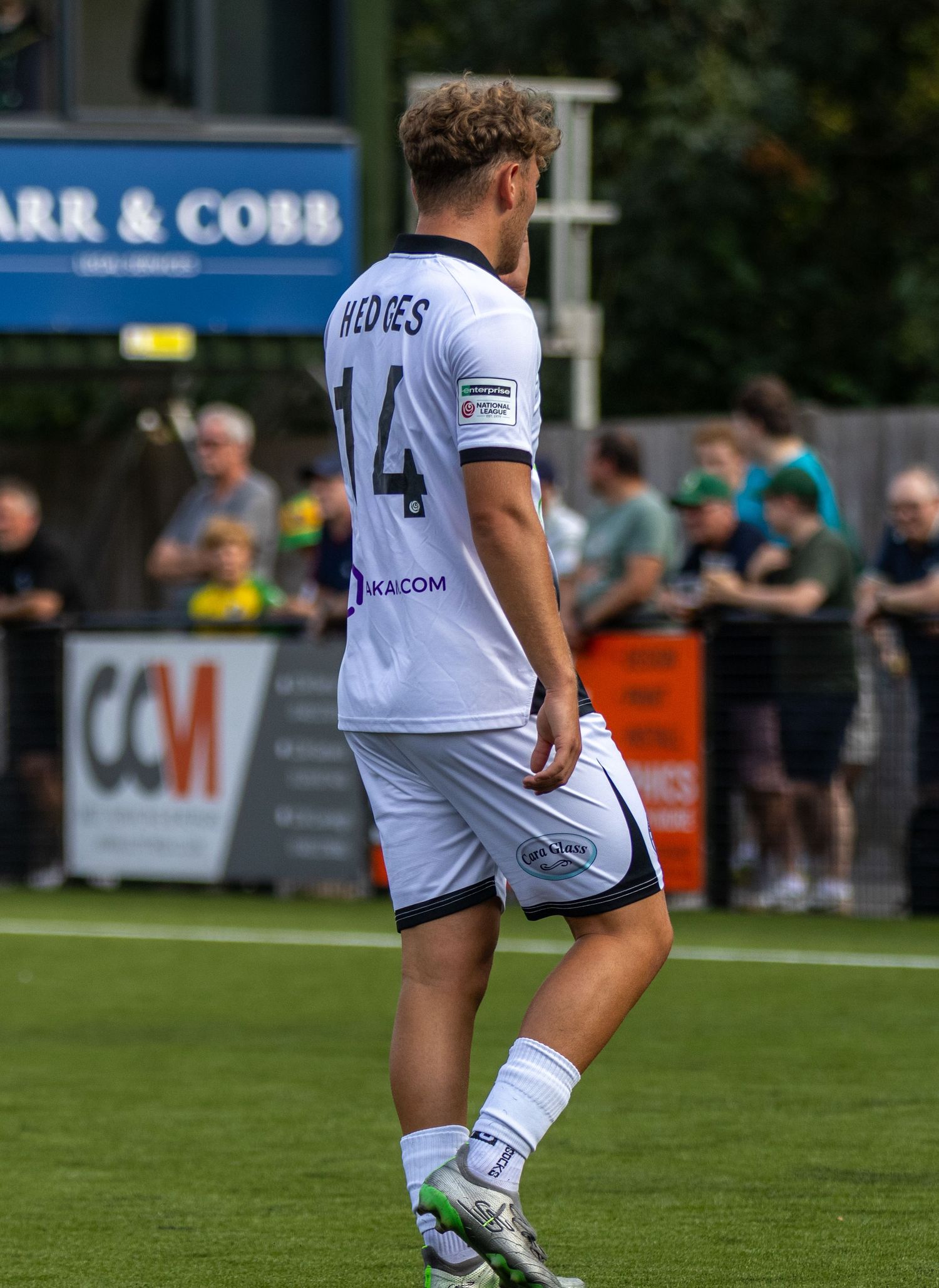 Football player number 14 Hayes in white kit stands on the pitch at a Carr & Cobb sponsored stadium.