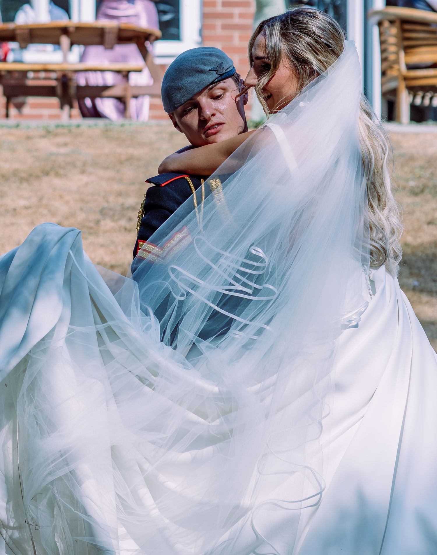 Bride and groom in military uniform sharing an intimate moment under a flowing white veil outdoors.