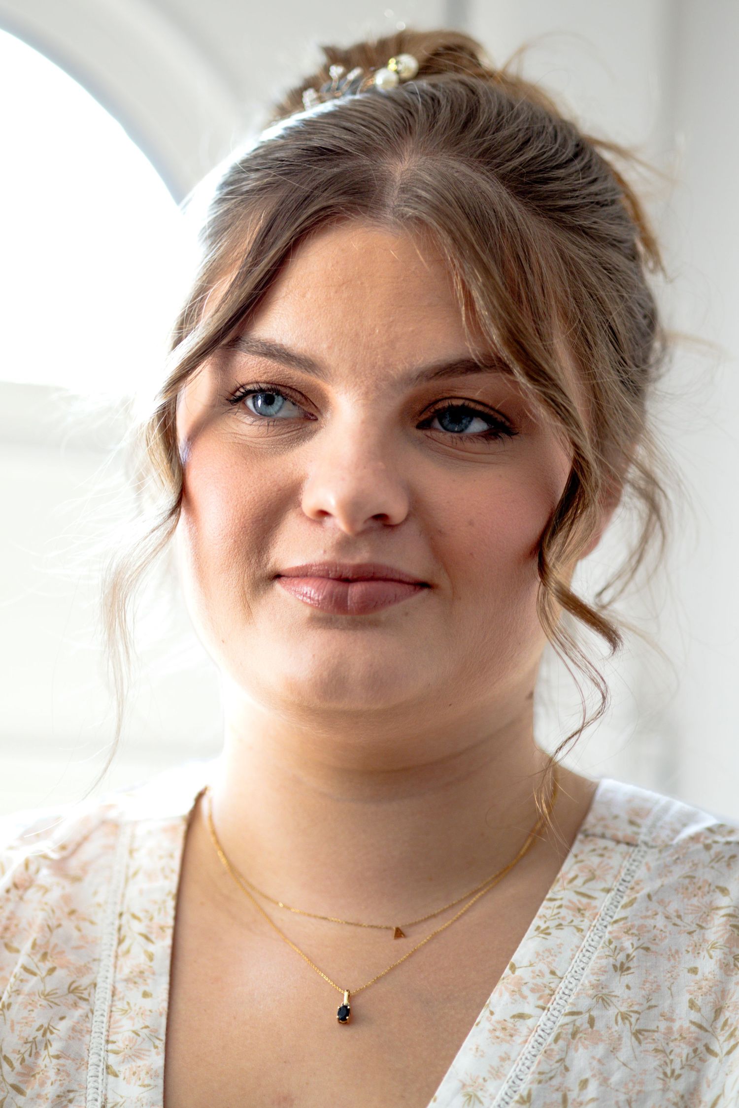 Young woman with updo hairstyle and delicate necklace smiling softly at wedding event.