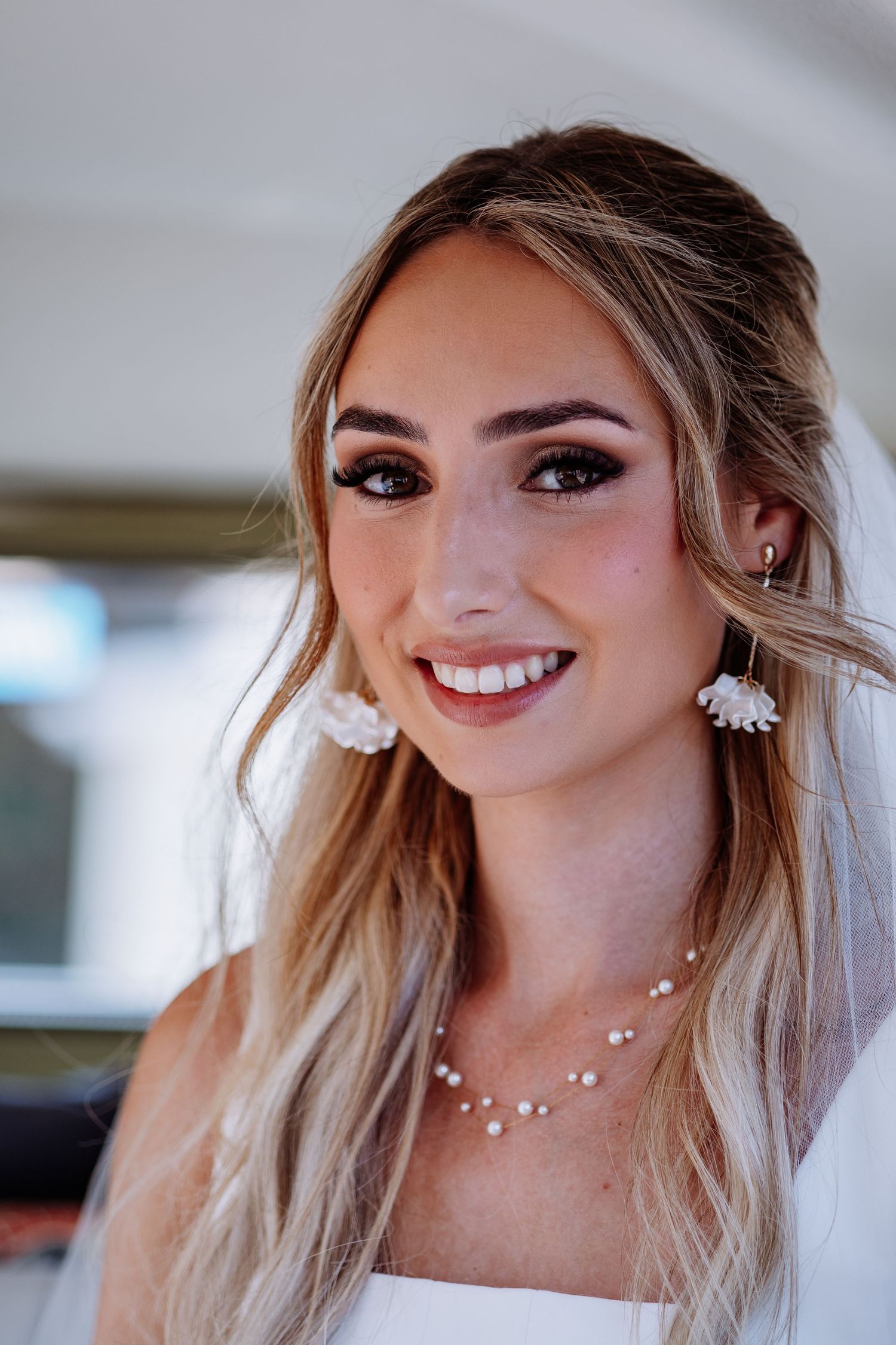 Close-up portrait of a smiling bride wearing floral earrings and pearl necklace with elegant bridal makeup.