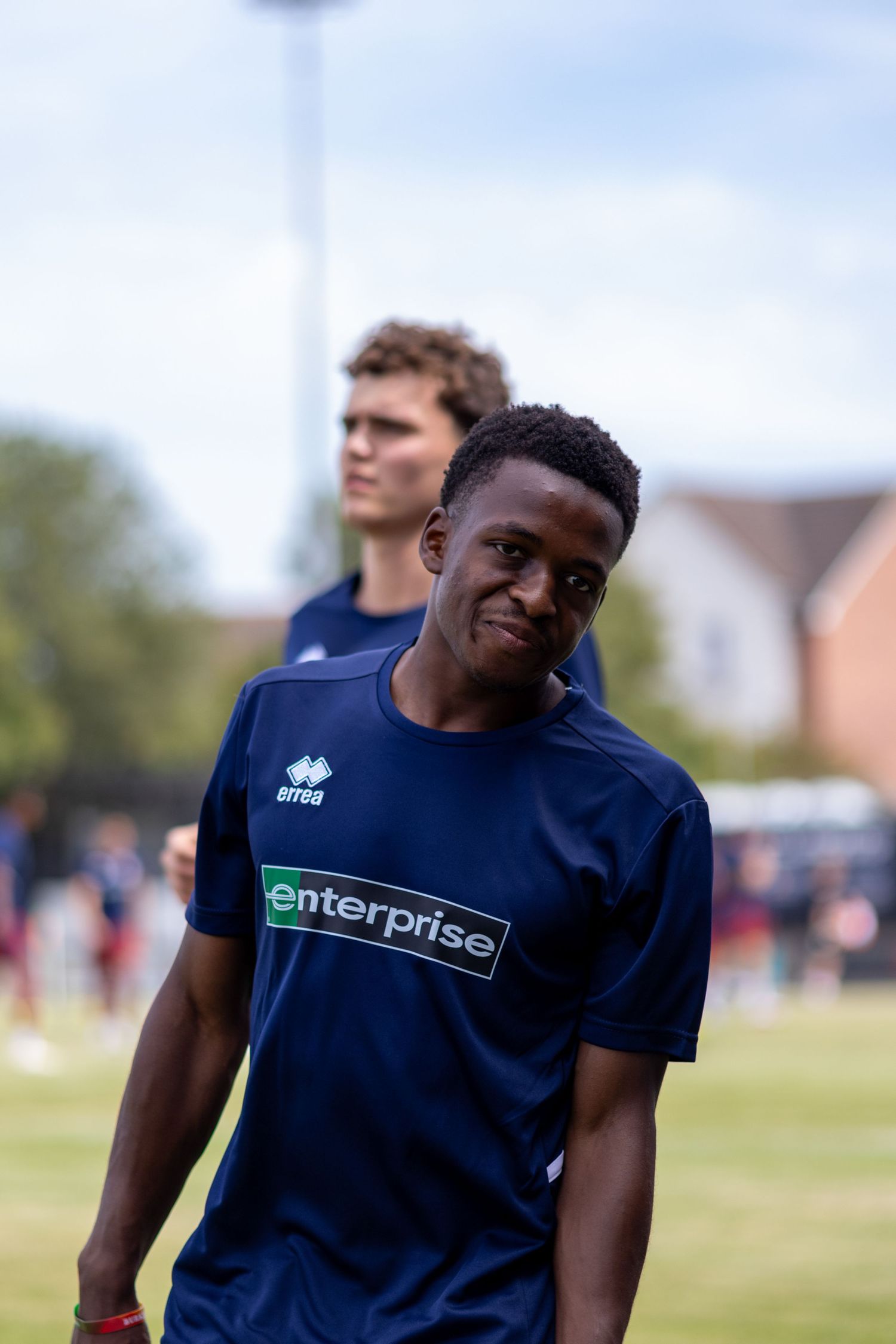 Young Black footballer in navy Enterprise-sponsored Errea shirt smiling during outdoor training session.