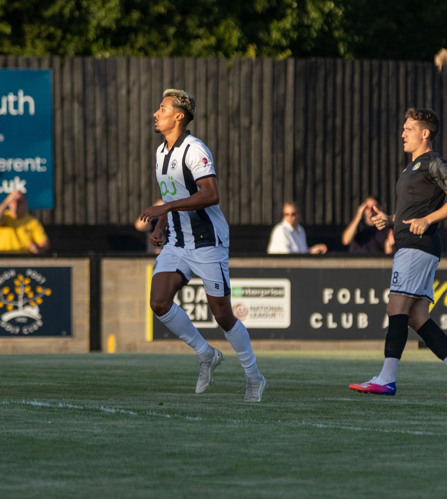 A footballer wearing number 13 in black and white kit sprints during a competitive match at a non-league ground.