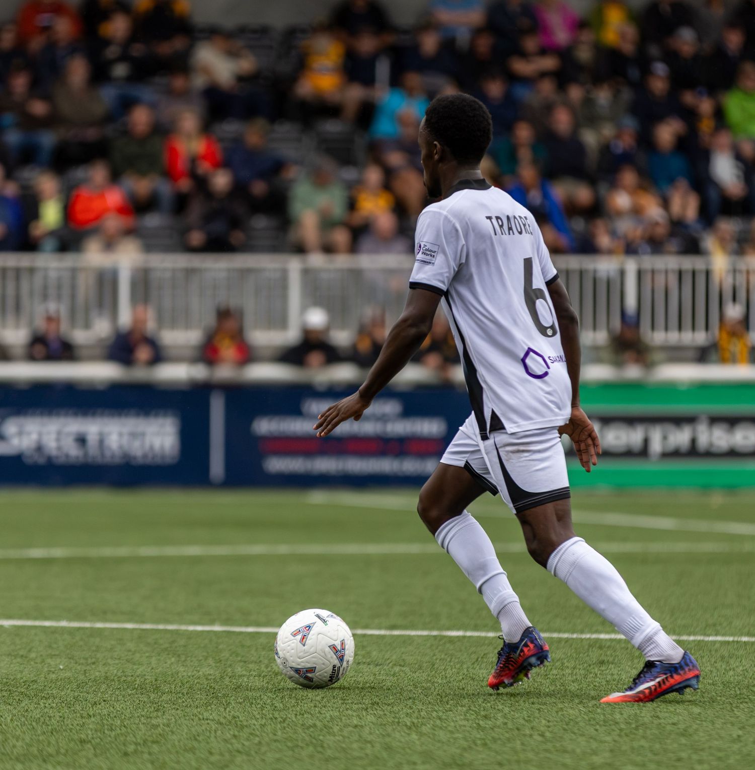 Soccer player Traore wearing number 6 white jersey dribbles ball on green field during competitive match.