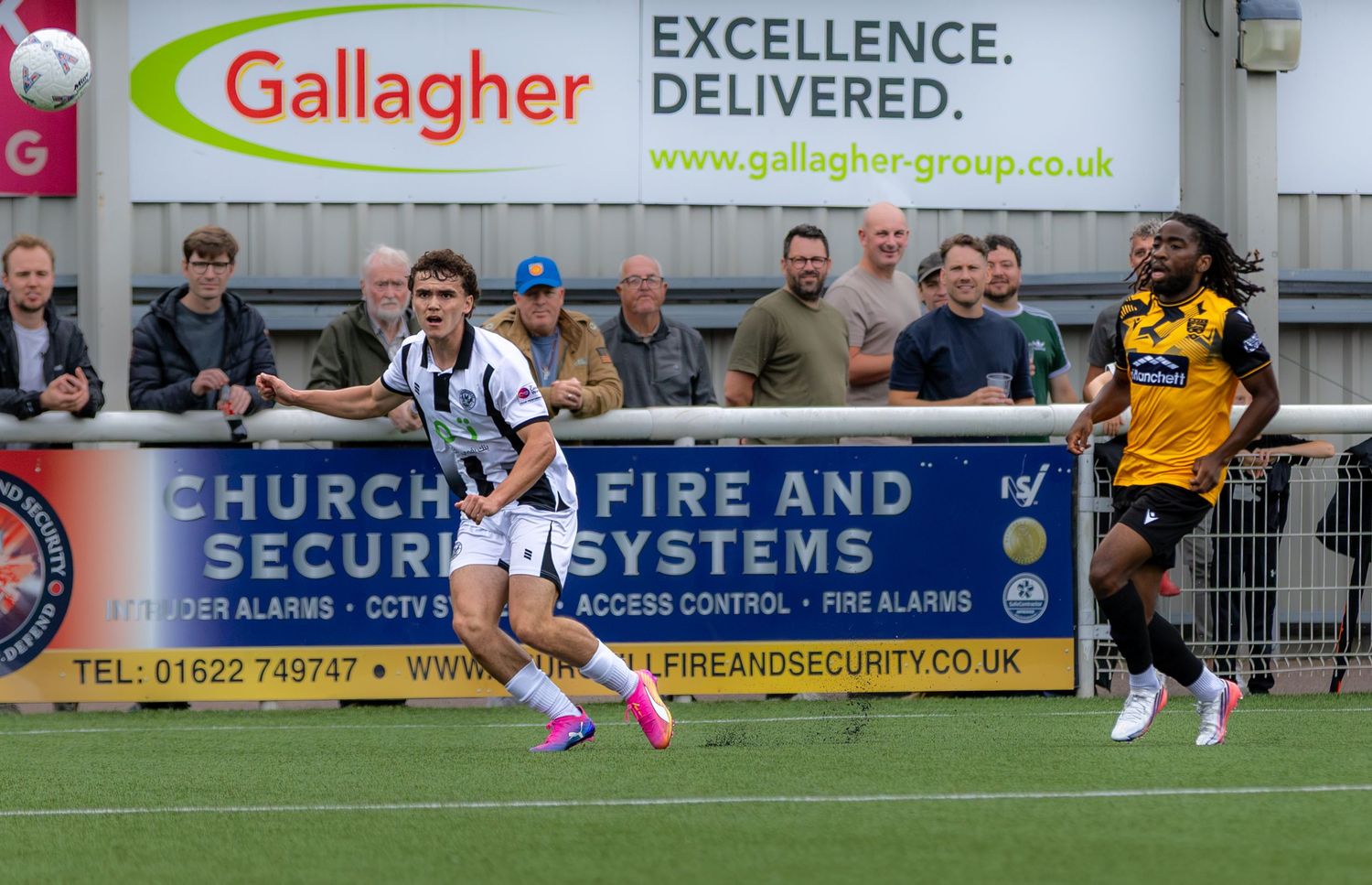 Two soccer players compete on the field near a Gallagher Excellence Delivered advertising board during a match.