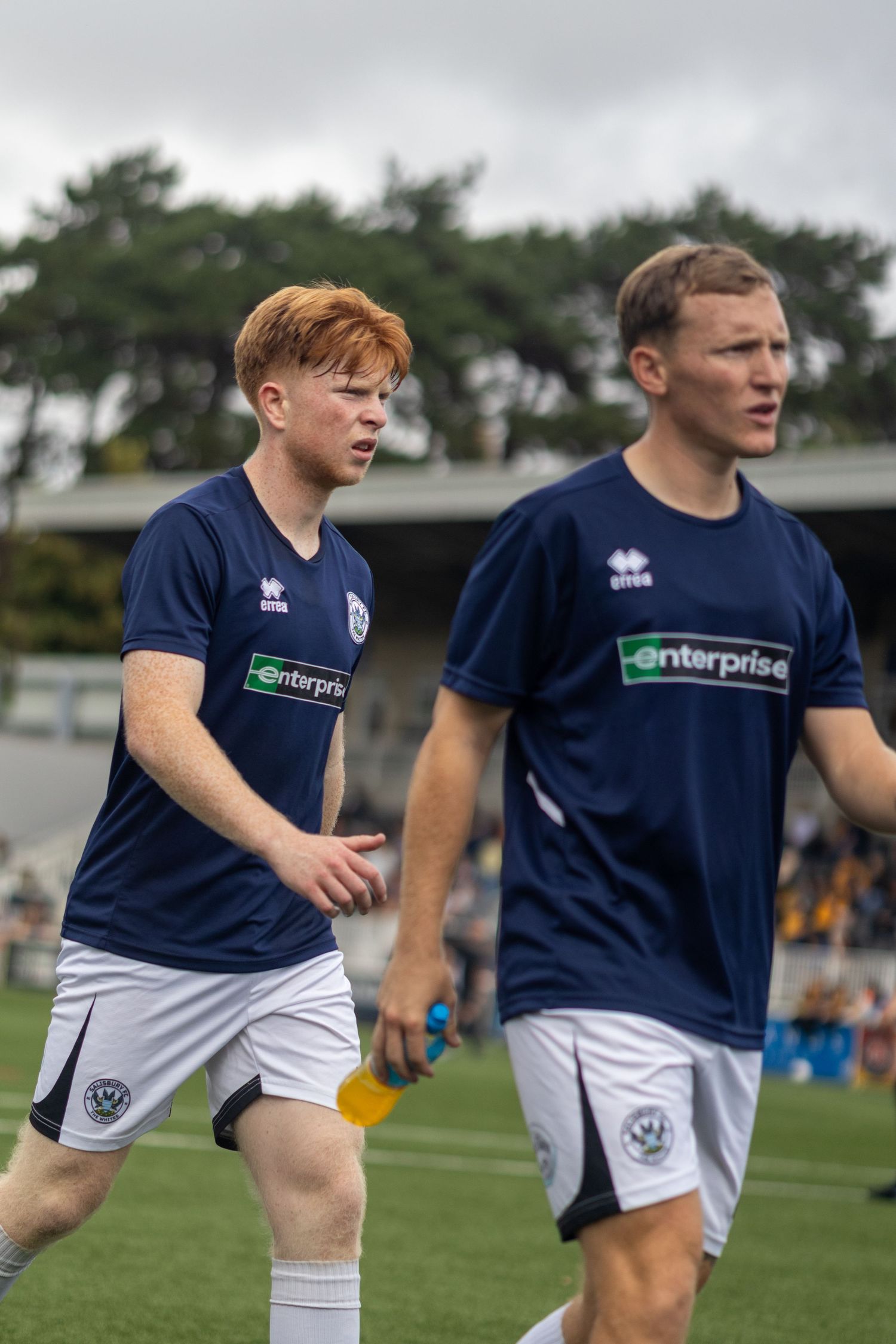 Two young soccer players in navy Enterprise-sponsored uniforms walk on a green pitch during a match.